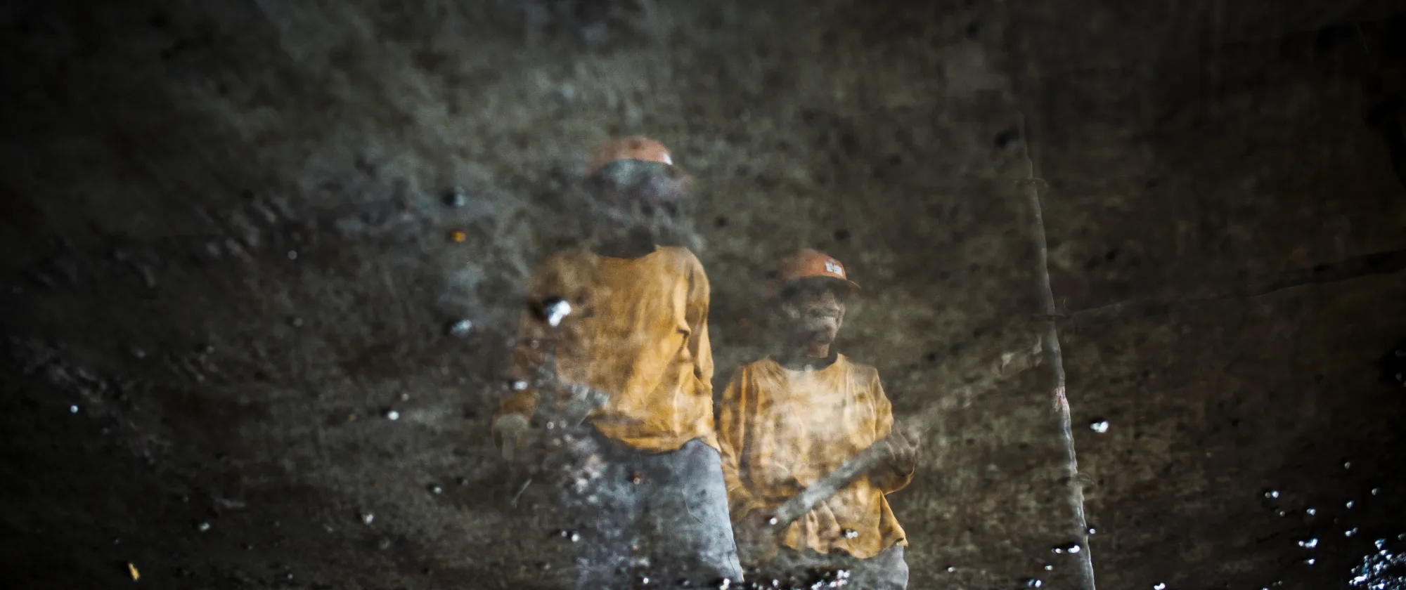 The mirrored reflection of two Malagasy construction workers captured in a puddle of water.