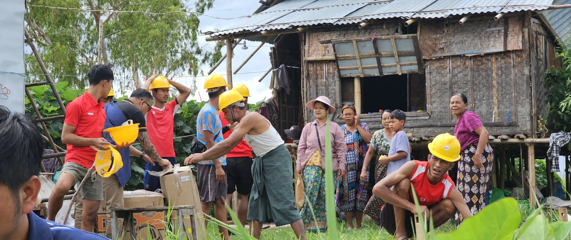 Community members wearing hard yellow hats are participating in rebuilding destroyed buildings