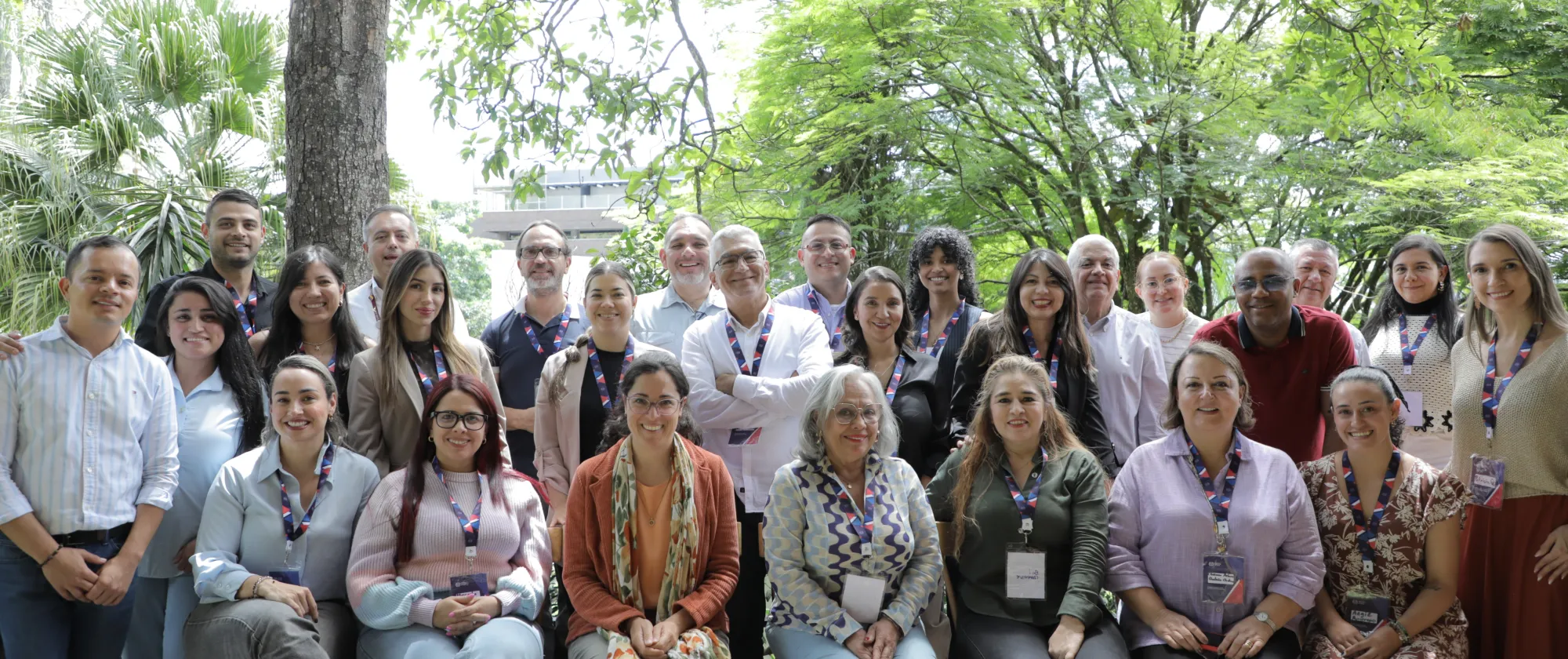 Group photo of the programme’s participants – more than 20 people smiling while posing in a green outdoor area.