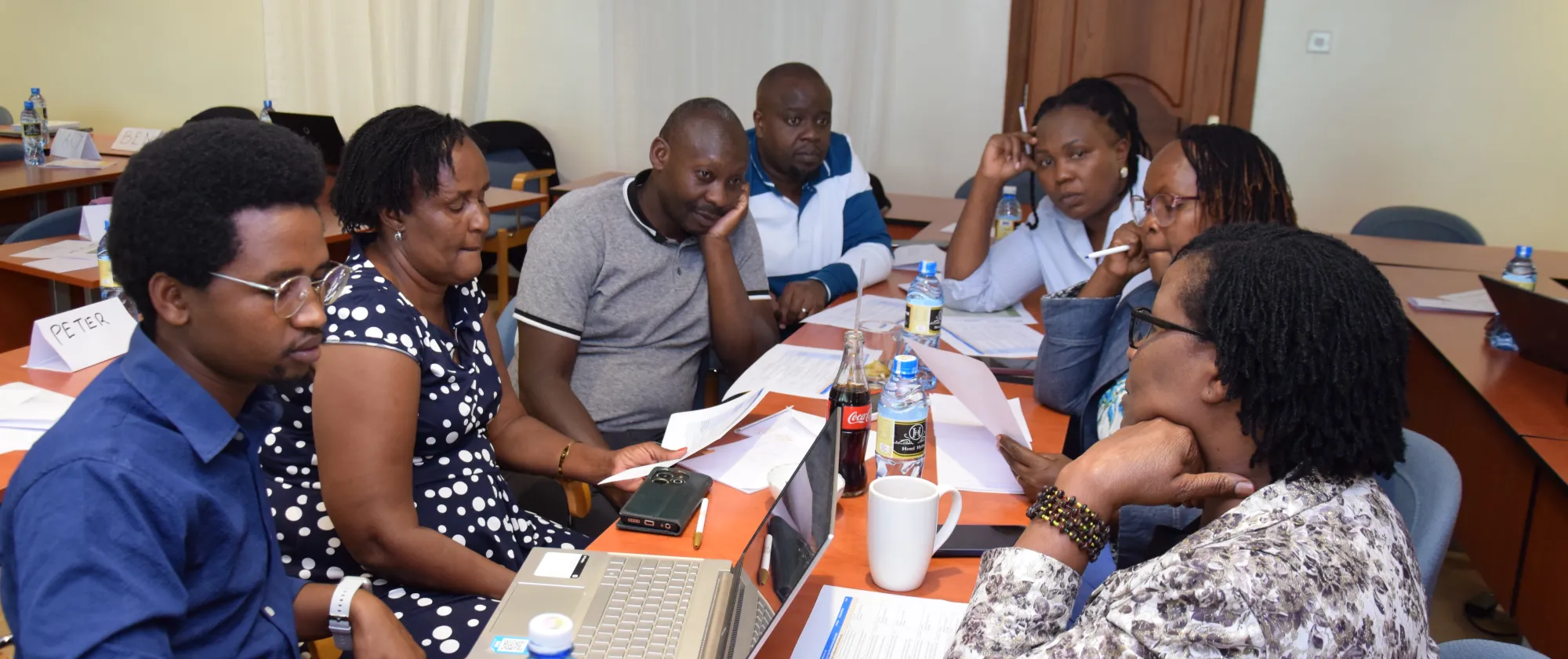 A group of men and women seated around a table, some looking at documents and laptops, during a gender analysis workshop in Kenya.
