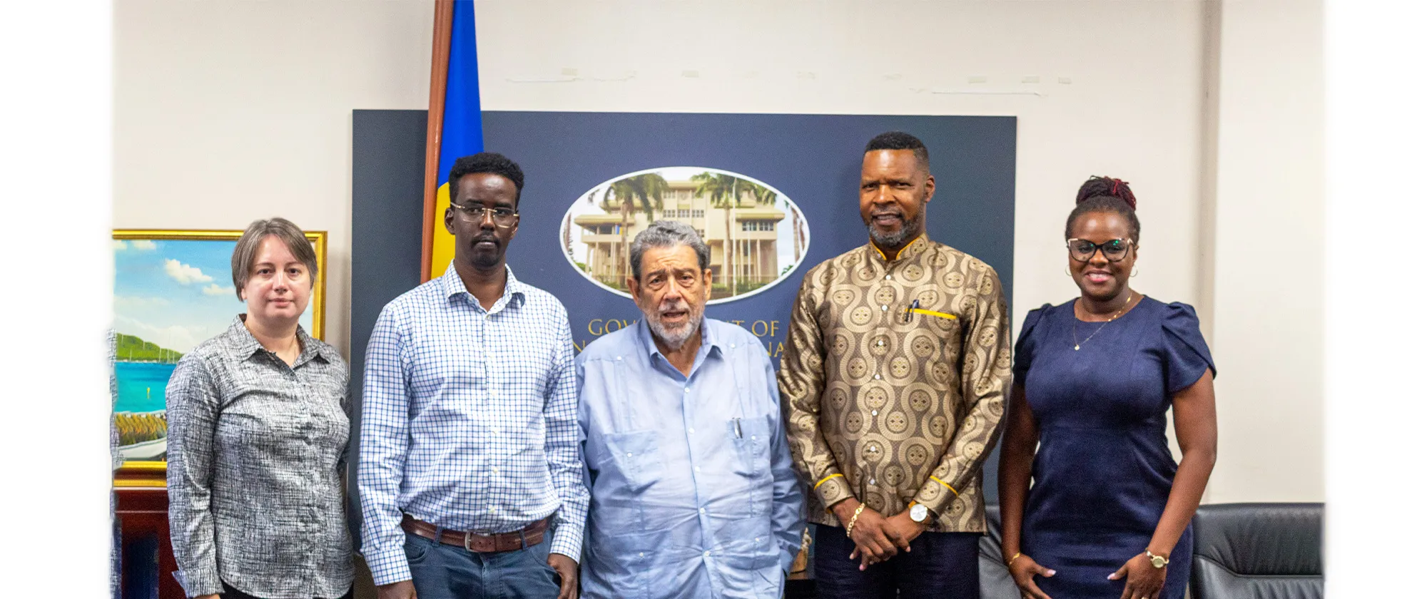 Group photo of five people standing indoors in front of a display with the words 'Government of Saint Vincent and the Grenadines.