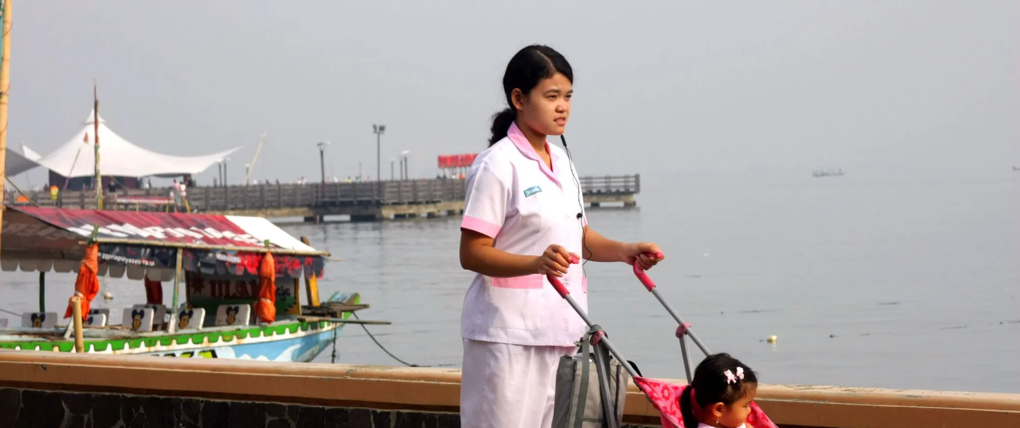 a babysitter pushing a baby cart with a toddler inside 