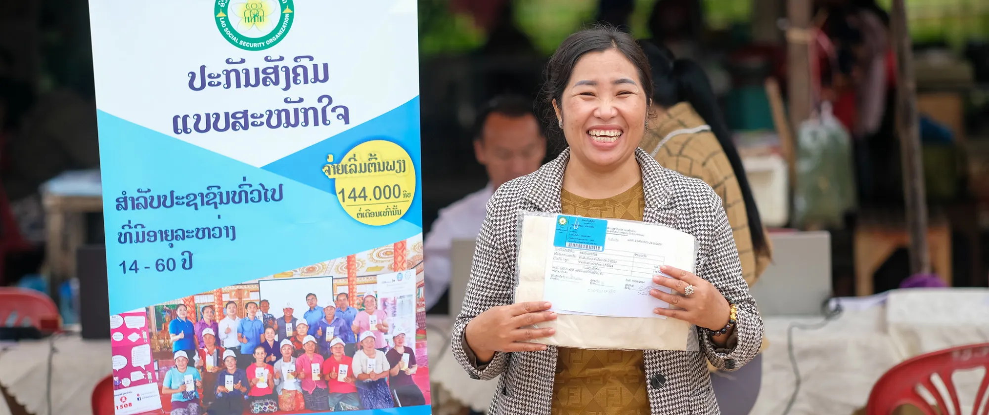 A smiling woman holding a document stands in front of a promotional standee.