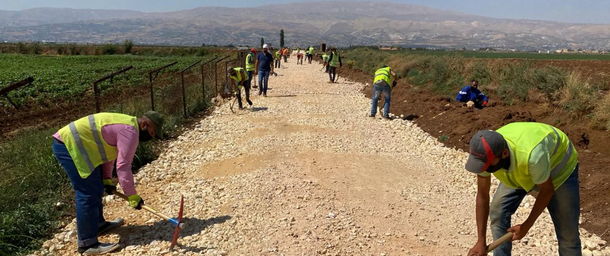 Several men wearing yellow vests work to rehabilitate rural road using hand tools