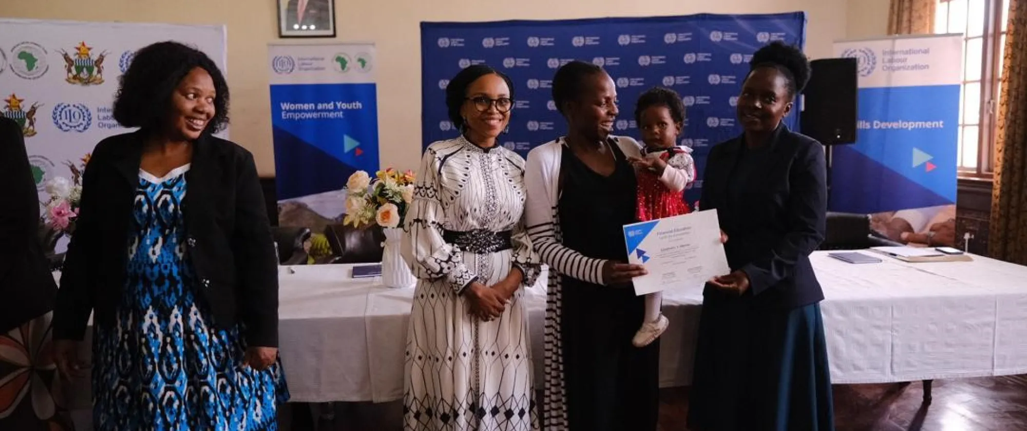 Line up of officials at the certificate handover ceremony with a trainer receiving carrying her baby