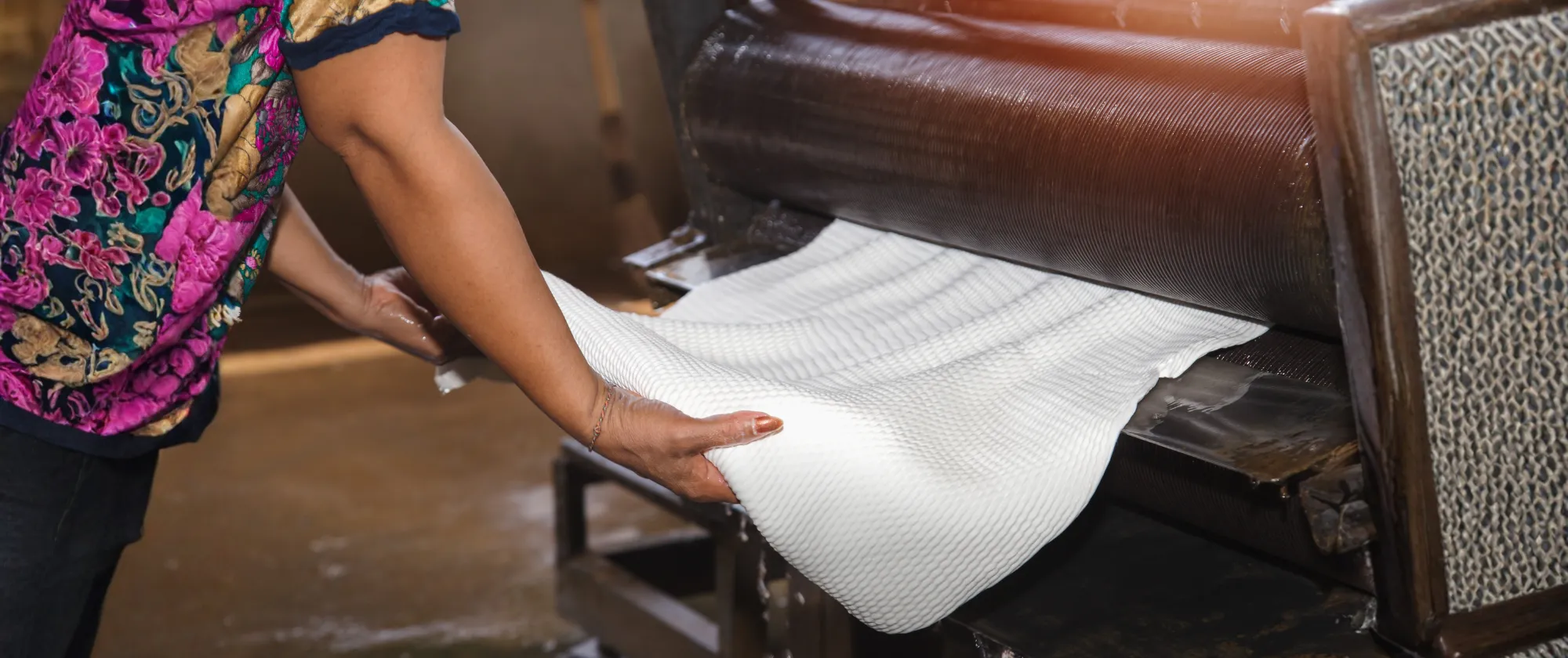 A worker operates a machine to press rubber sheets in a rubber factory.
