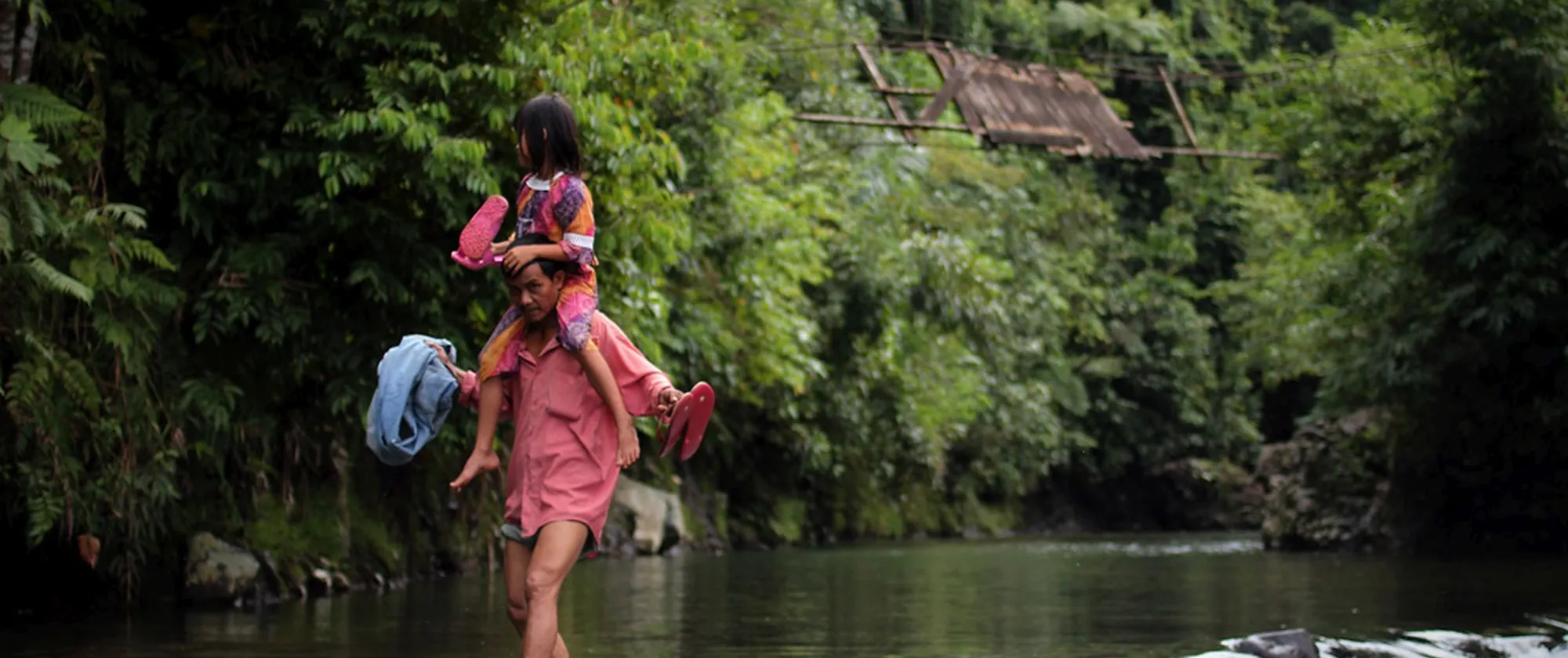 father and his daughter crossing a river in a forest