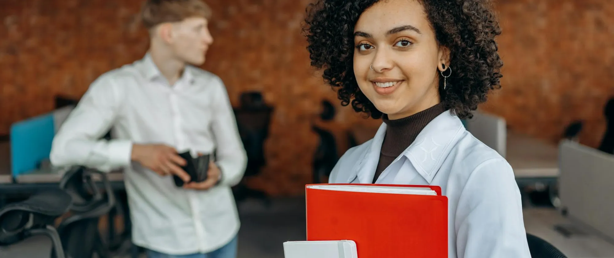 Young woman in white long sleeve shirt holding financial book report and standing with her colleagues inside an office