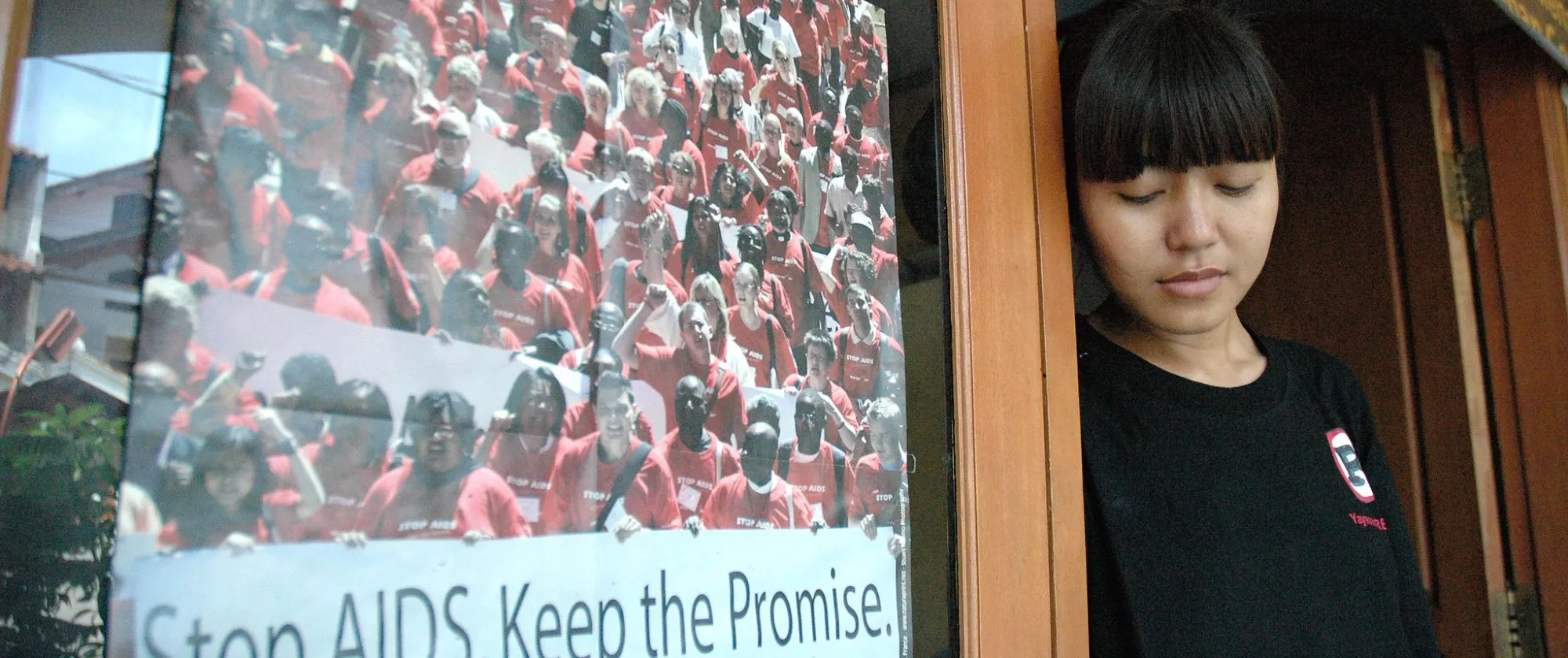 a girl in black t-shirt side by side with a poster "Stop AIDS. Keep the promise".