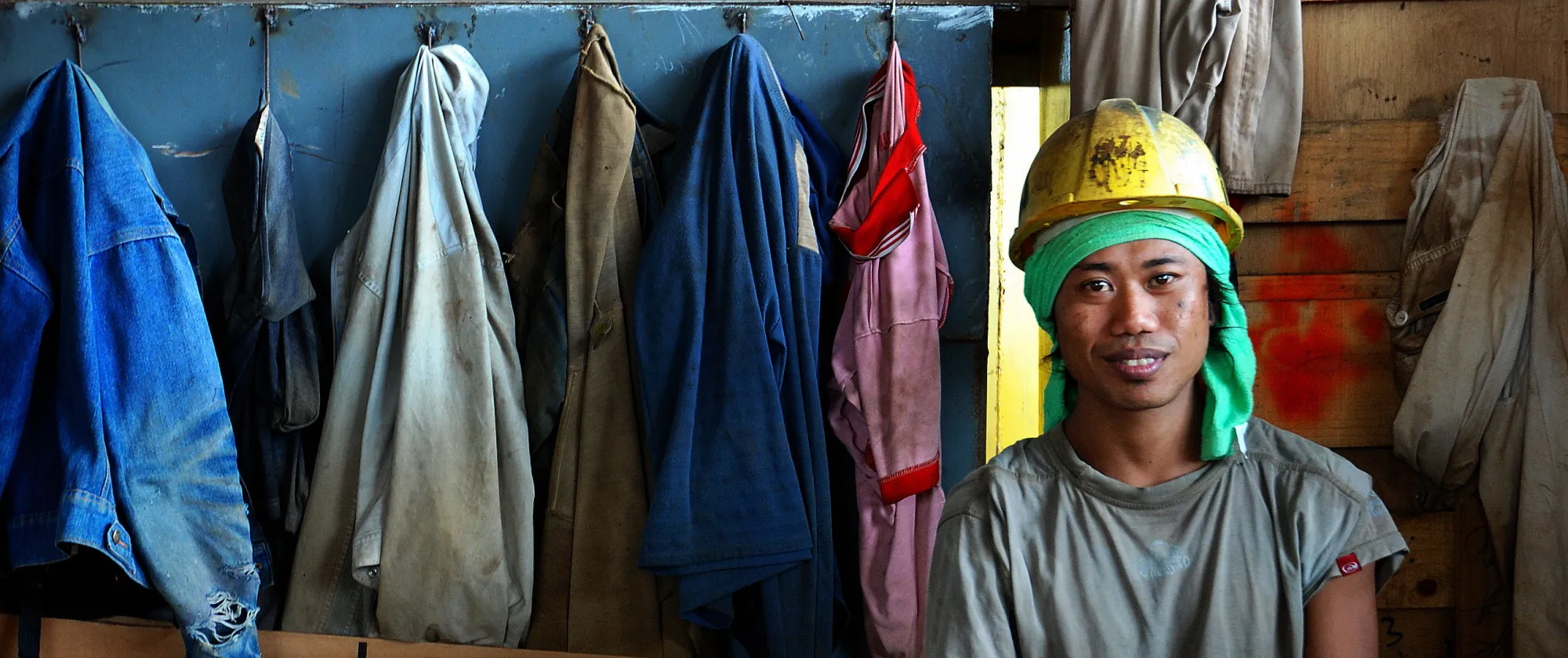 Worker wearing a helmet sitting against a wall in workers coat room