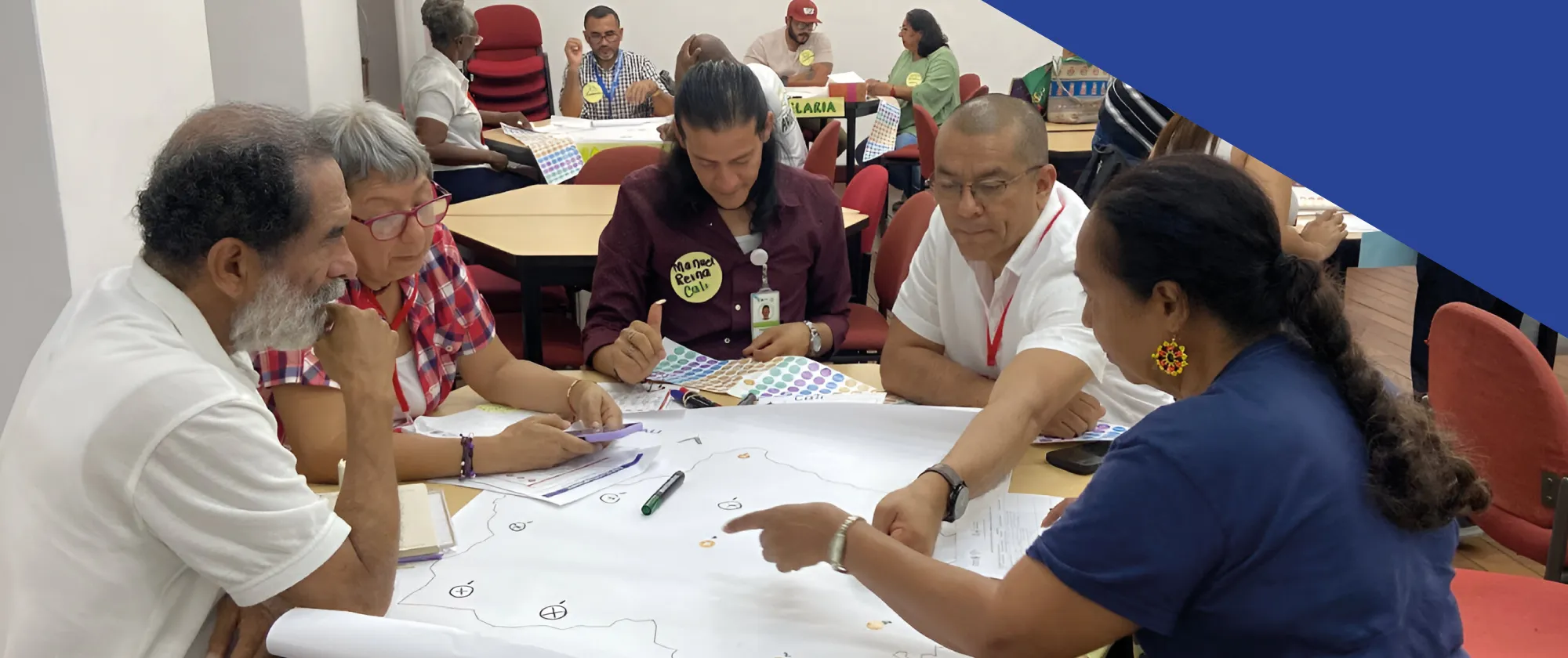 Cinco personas adultas sentadas alrededor de una mesa revisan y señalan un mapa sobre papel grande, con marcadores y hojas dispersas.