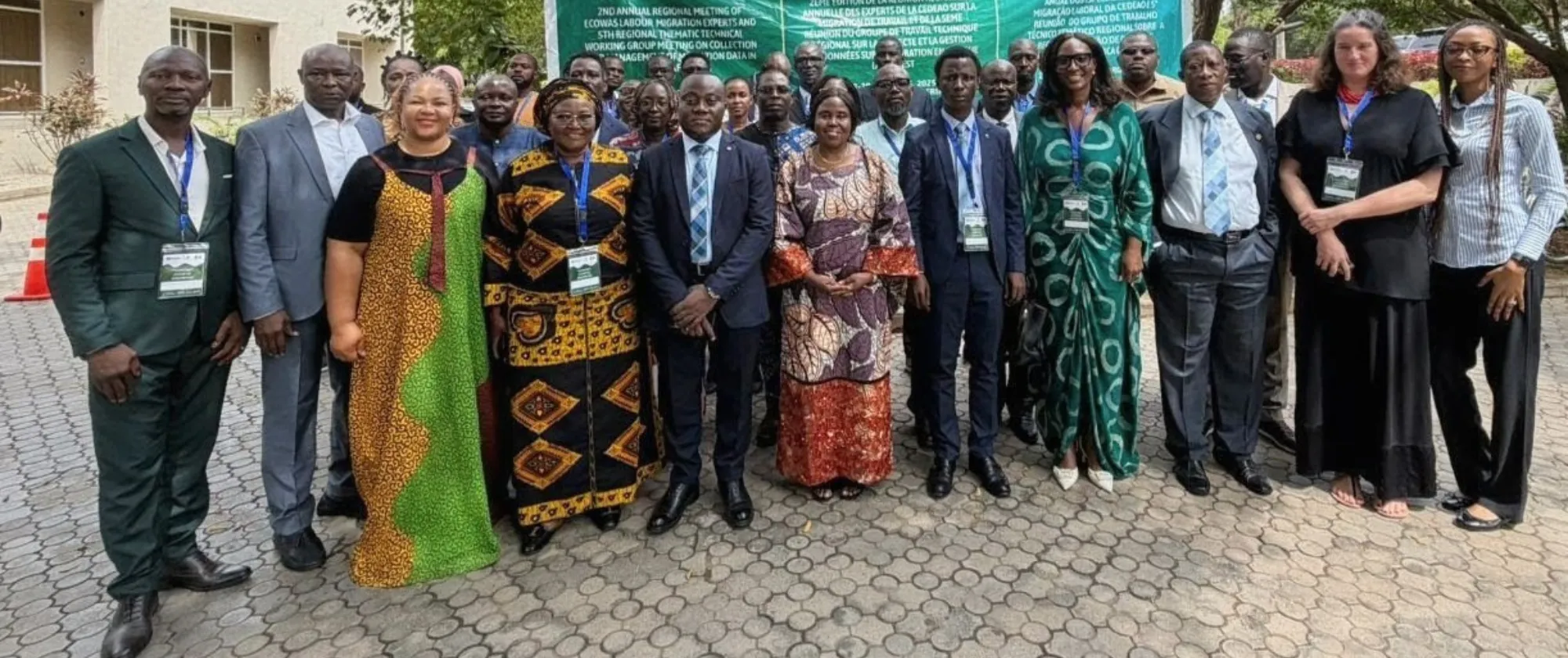 The photo captures a group of delegates standing outdoors in front of a large green banner