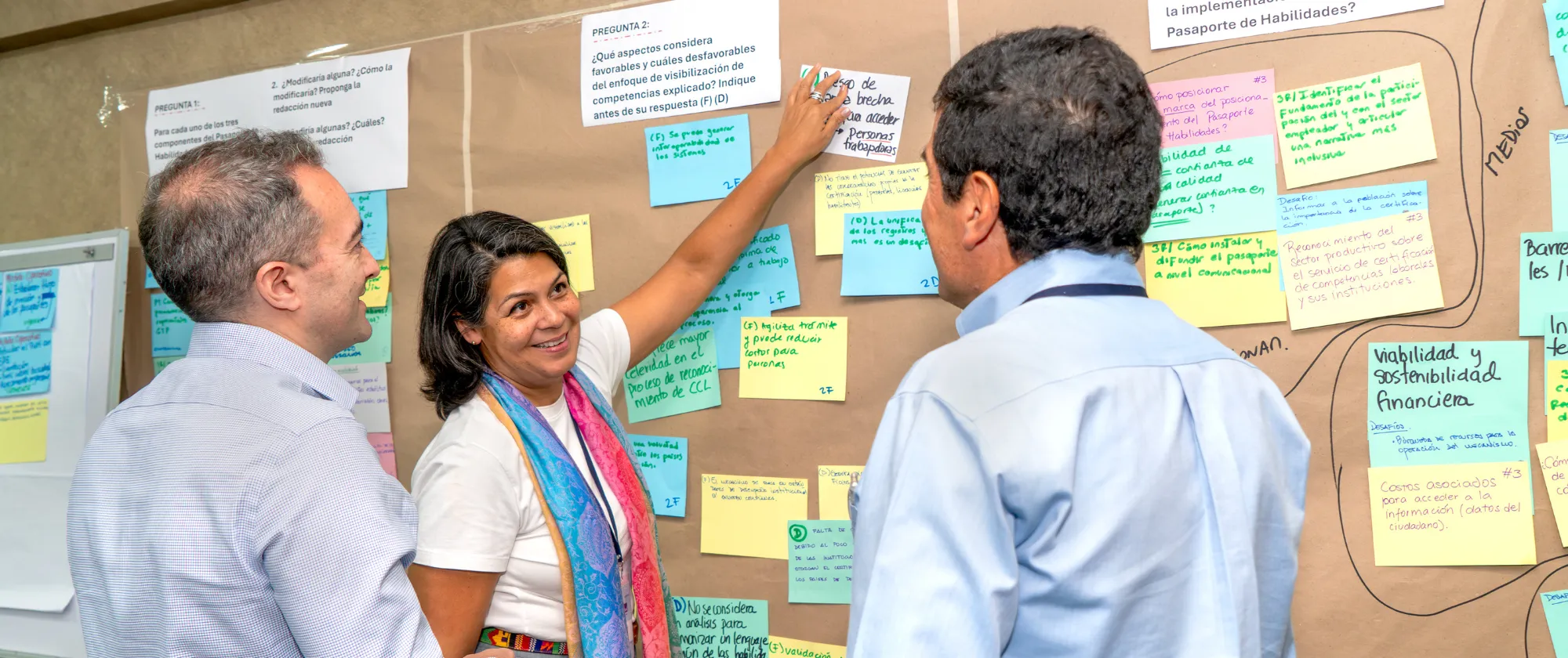 Tres personas interactúan en la construcción de un mural con información.