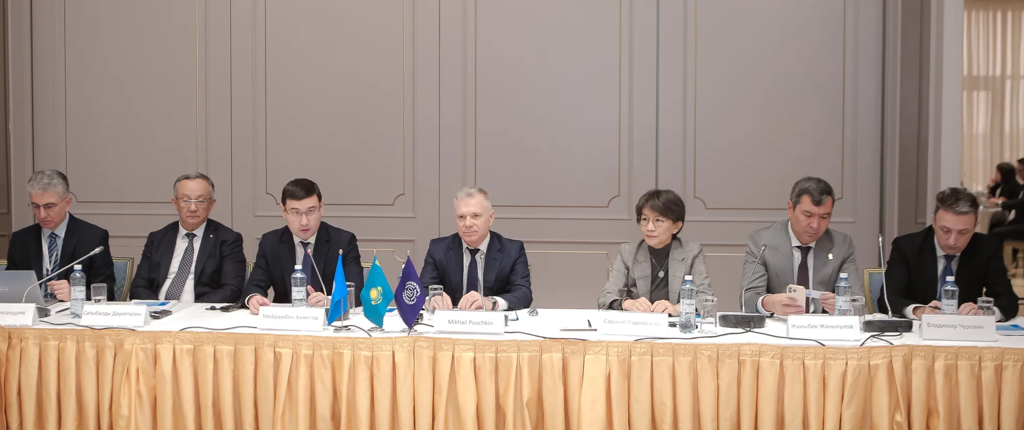 Seven panellists seating behind a long table with nameplates and microphones