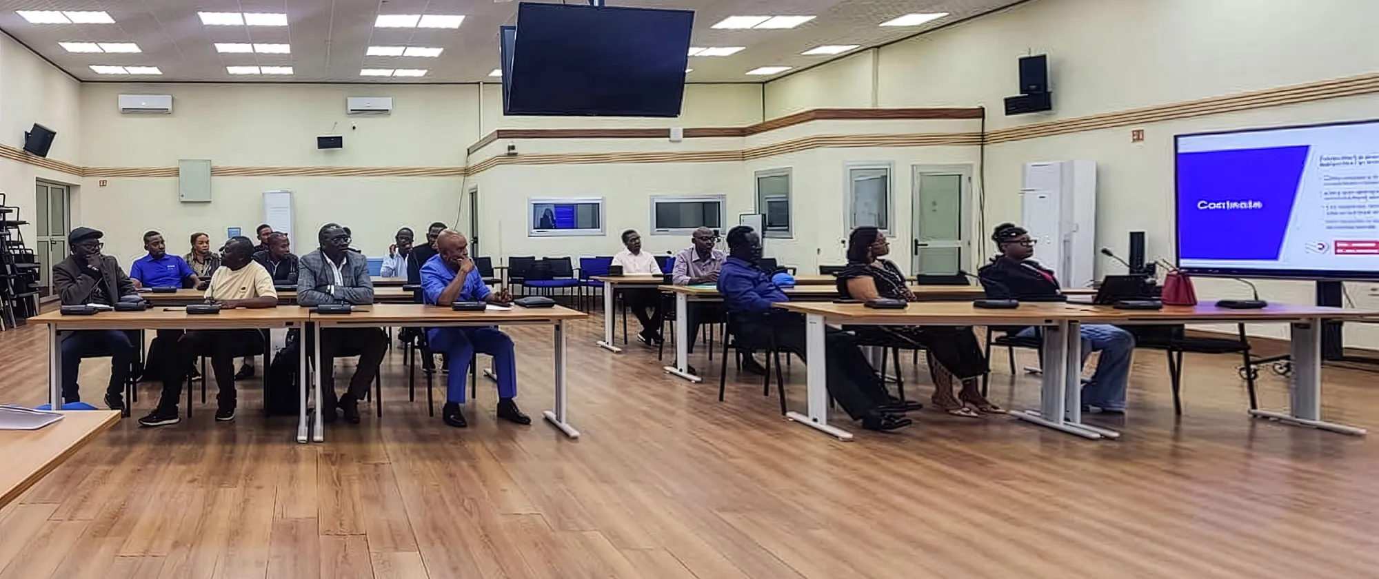 Participants basés à Kinshasa assistent à une séance d’information dans une salle de réunion, assis autour de tables et suivant une présentation projetée à l’écran.