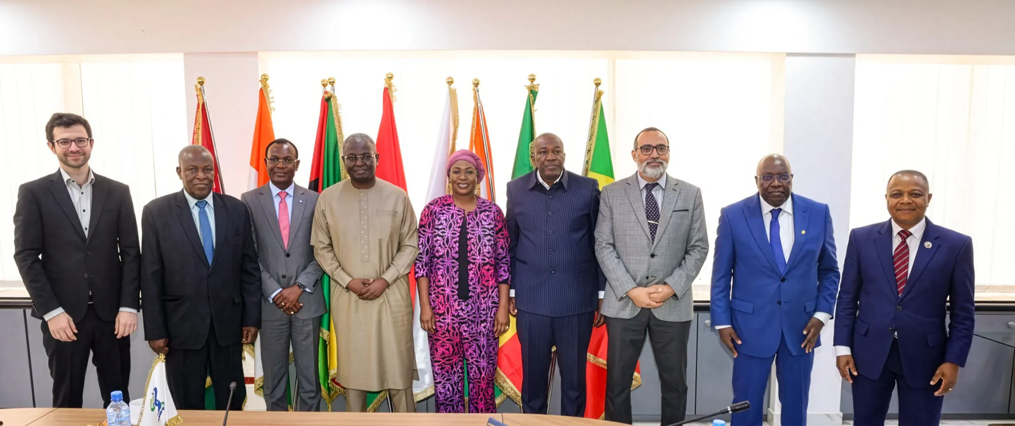 Photo de groupe montrant les délégations de l’OIT et de l’UEMOA alignées côte à côte lors d’une réunion officielle à Ouagadougou, avec les drapeaux des États membres de l’UEMOA en arrière-plan.