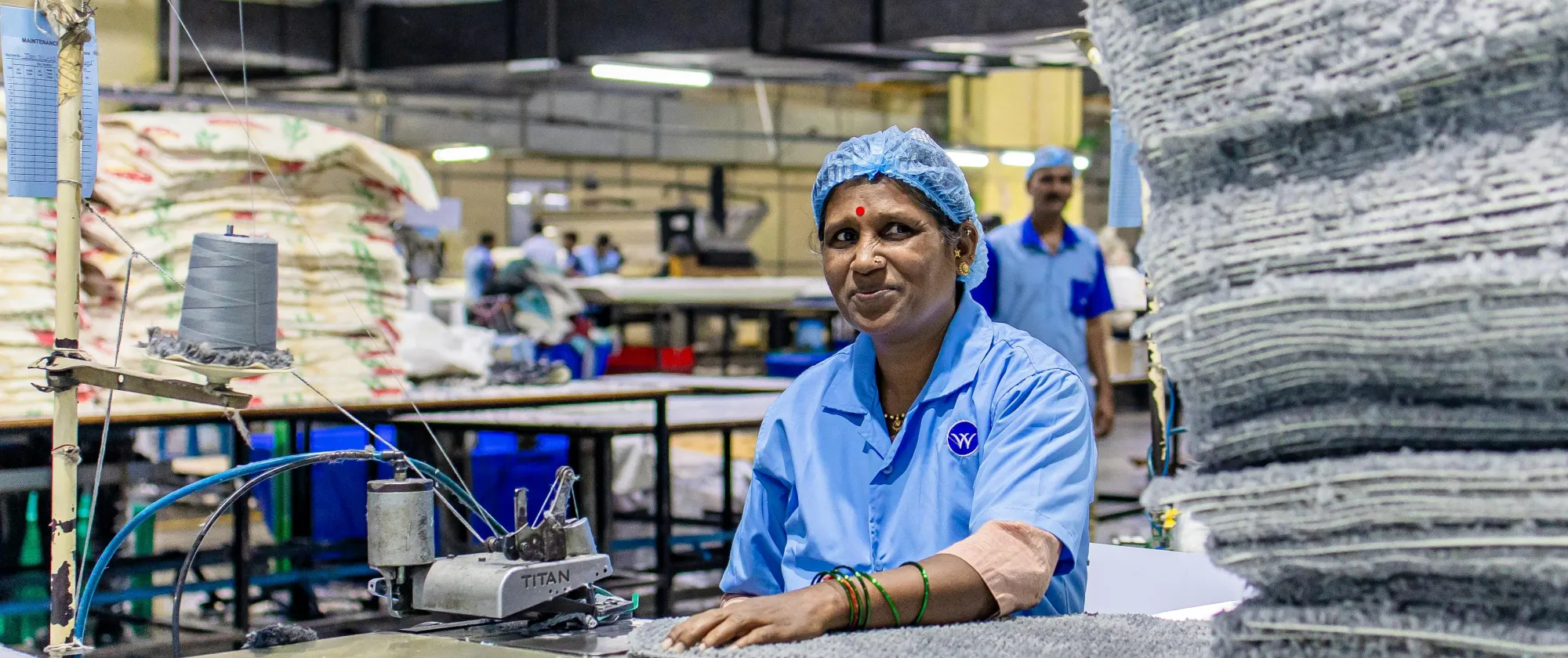 A woman in a blue uniform and hairnet smiles while working at a textile factory. 
