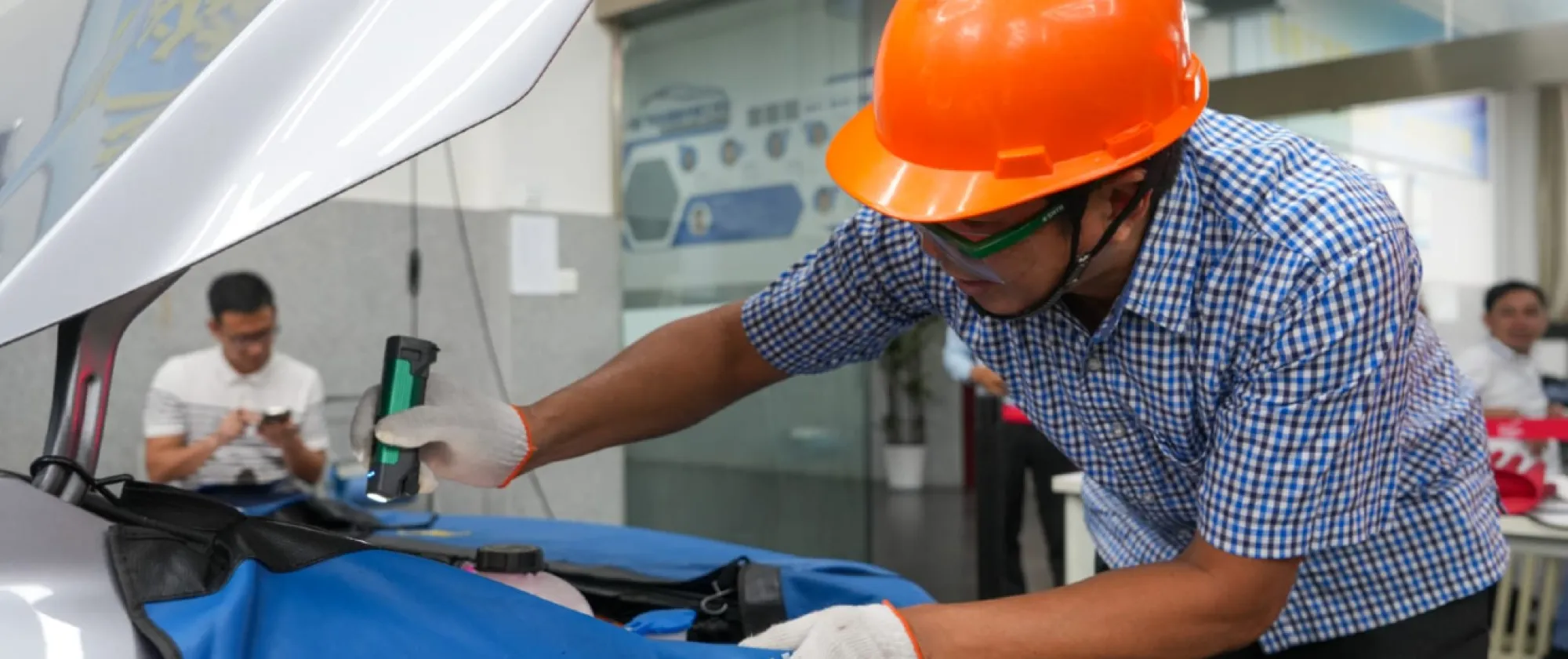 A man wearing an orange hard hat is working on a car engine.