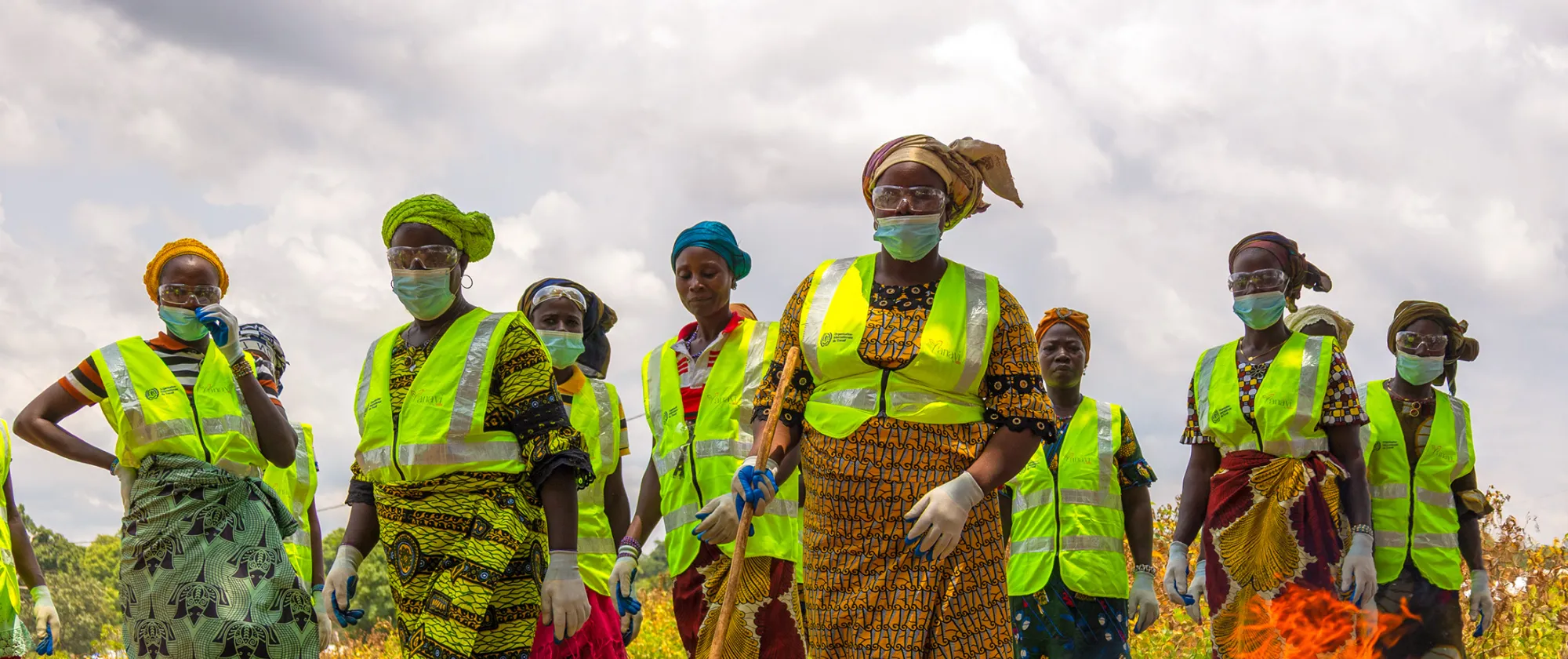 Des travailleuses agricoles en Côte d’Ivoire se tiennent dans un champ, portant des gilets de sécurité, des lunettes de protection, des masques et des gants, soulignant l’importance de conditions de travail sûres et respectueuses.