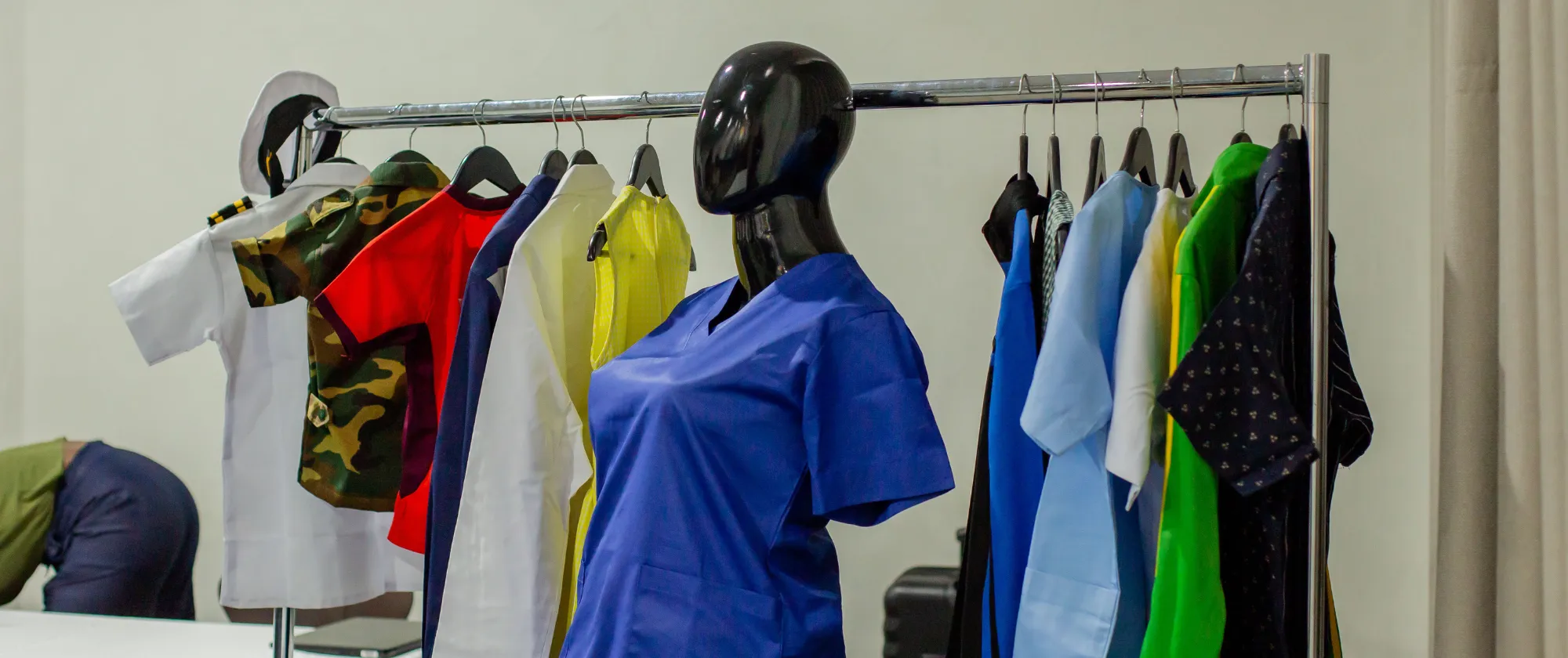 A mannequin and clothing rack displaying various garments, including uniforms and colorful apparel, at an indoor event