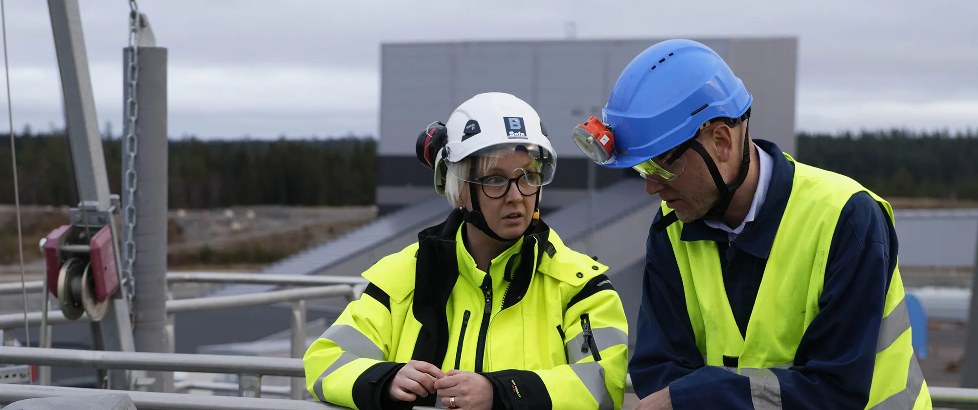 Two workers wearing helmets and yellow vests standing next to each other.