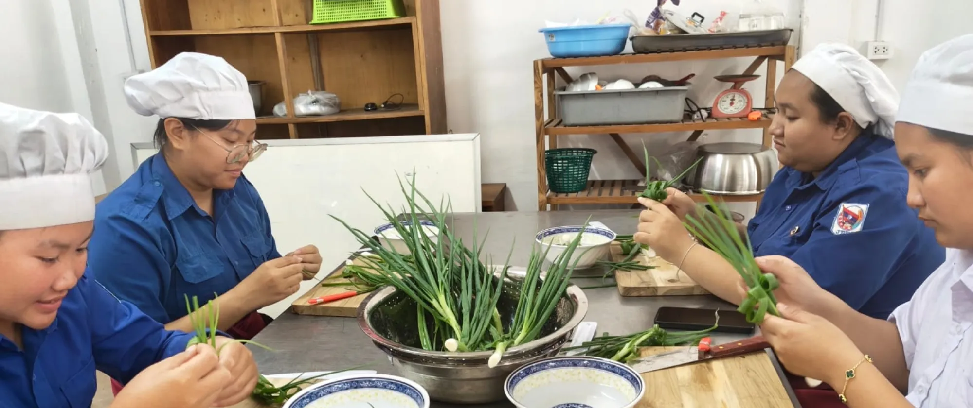 Women and men wearing white hats are preparing vegetables. 