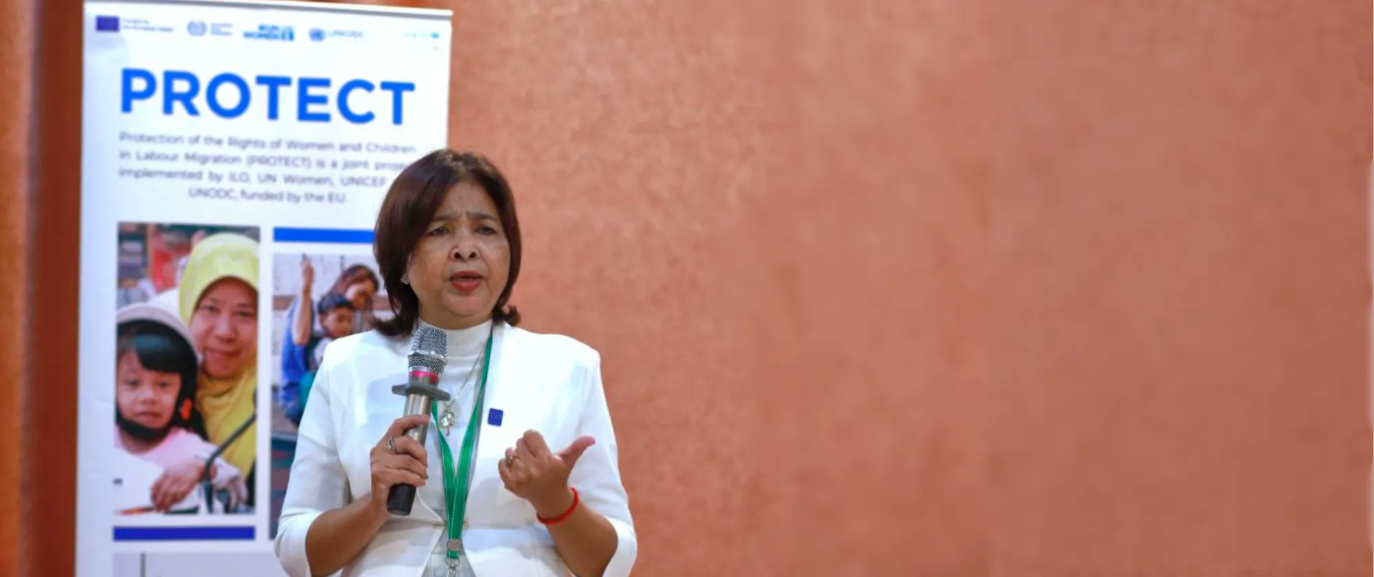 A lady holding a microphone speaks in front of a meeting room. 
