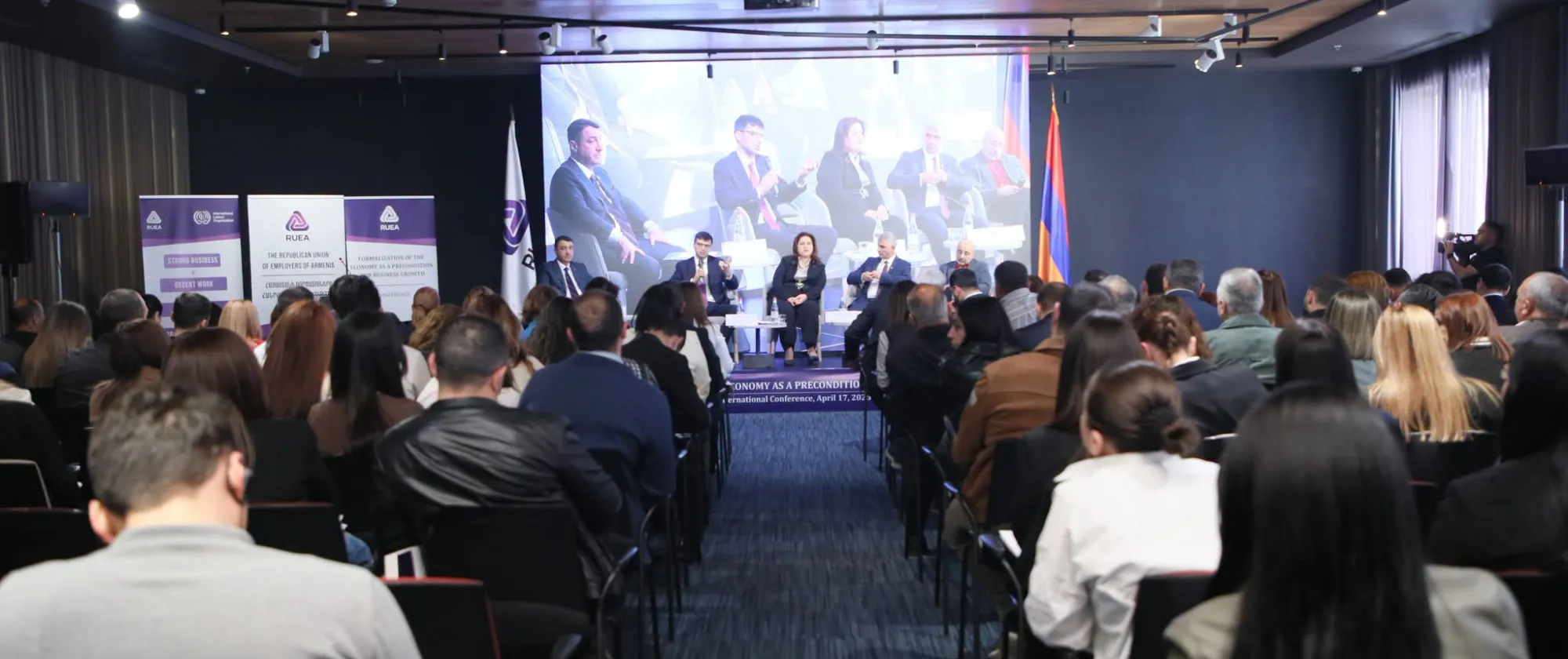 Audience seated facing speakers on stage