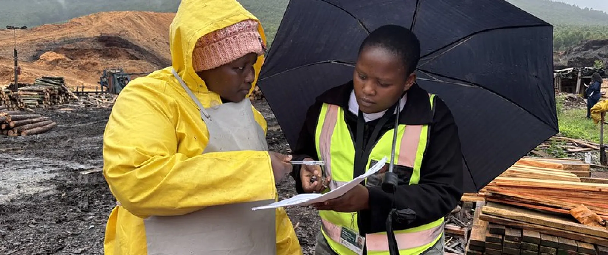 a woman conducting a survey to another woman at her workplace, which is a construction site; it's raining