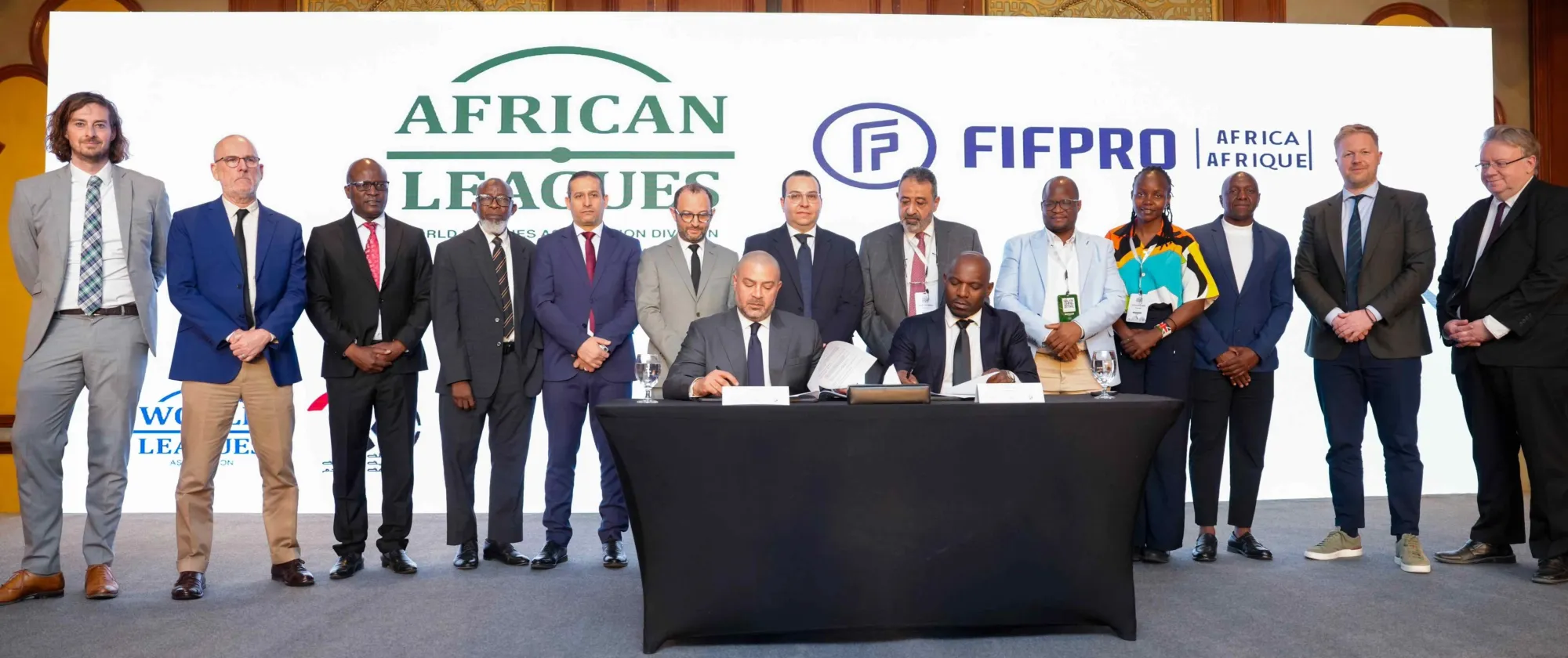 Group photo of representatives standing behind two seated signatories at a table during the launch event of the African Leagues in Cairo. Large screens in the background display the African Leagues and FIFPRO Africa logos.