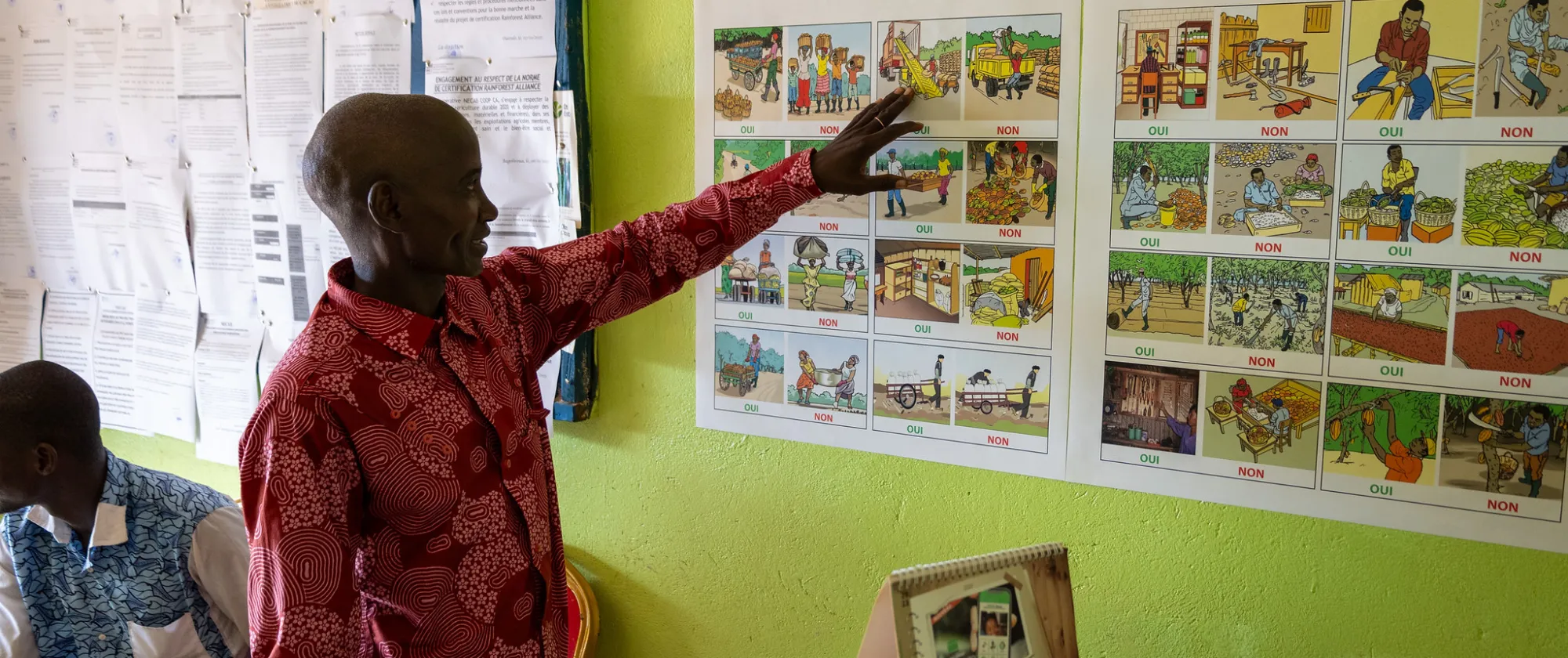 A cocoa farmer stands in front of two posters teaching.