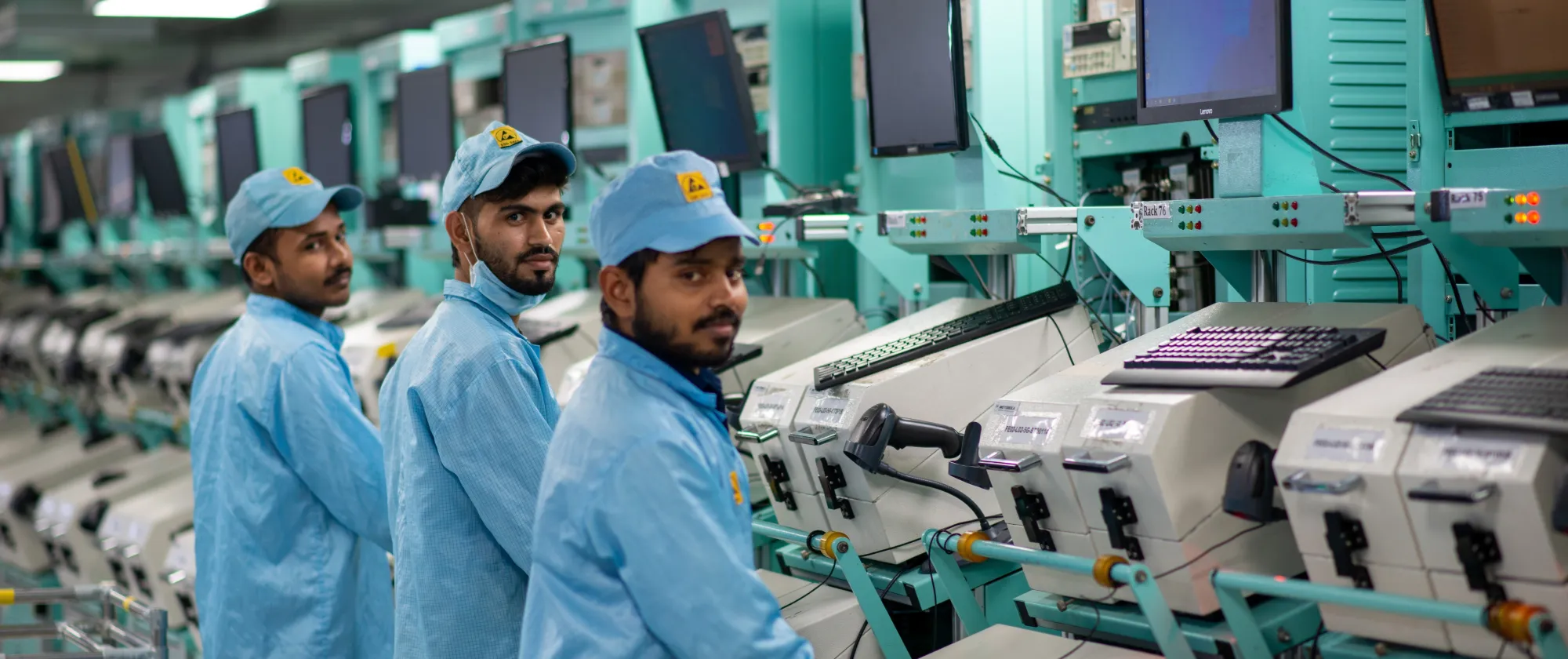 Three workers wearing blue uniforms are operating a machine.