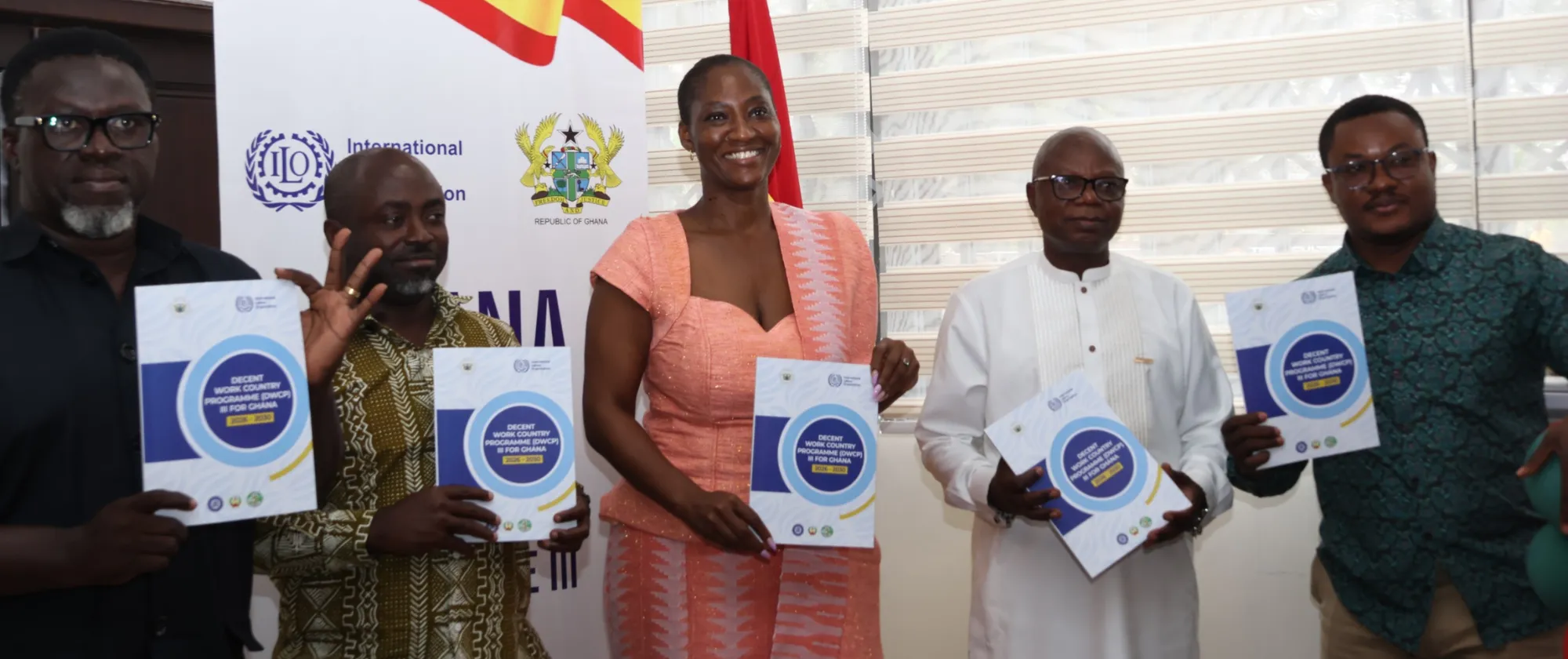 Five officials stand indoors holding copies of the Decent Work Country Programme document during a formal launch event.