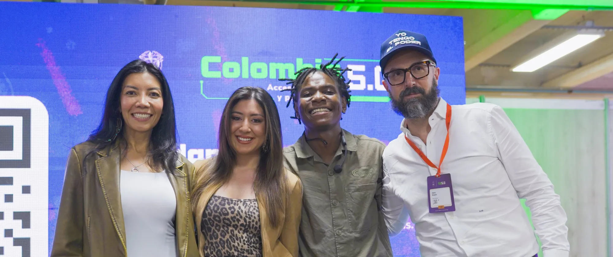 Una fotografía de cuatro personas sonriendo en un evento tecnológico. Están de pie una al lado de la otra frente a una gran pantalla azul que dice "Colombia 5.0" en verde y blanco.