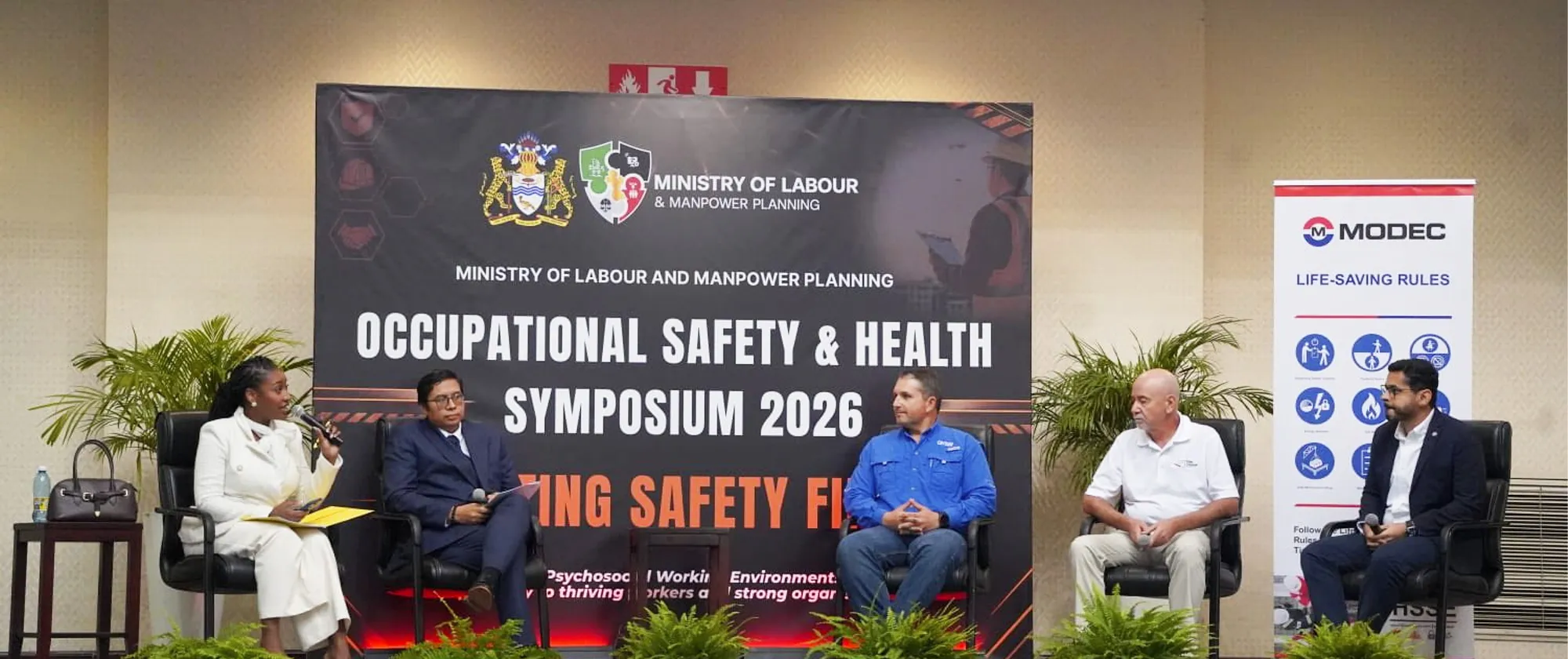 A panel of five professionals participates in a discussion on stage during the Occupational Safety & Health Symposium 2026, held by the Ministry of Labour and Manpower Planning.