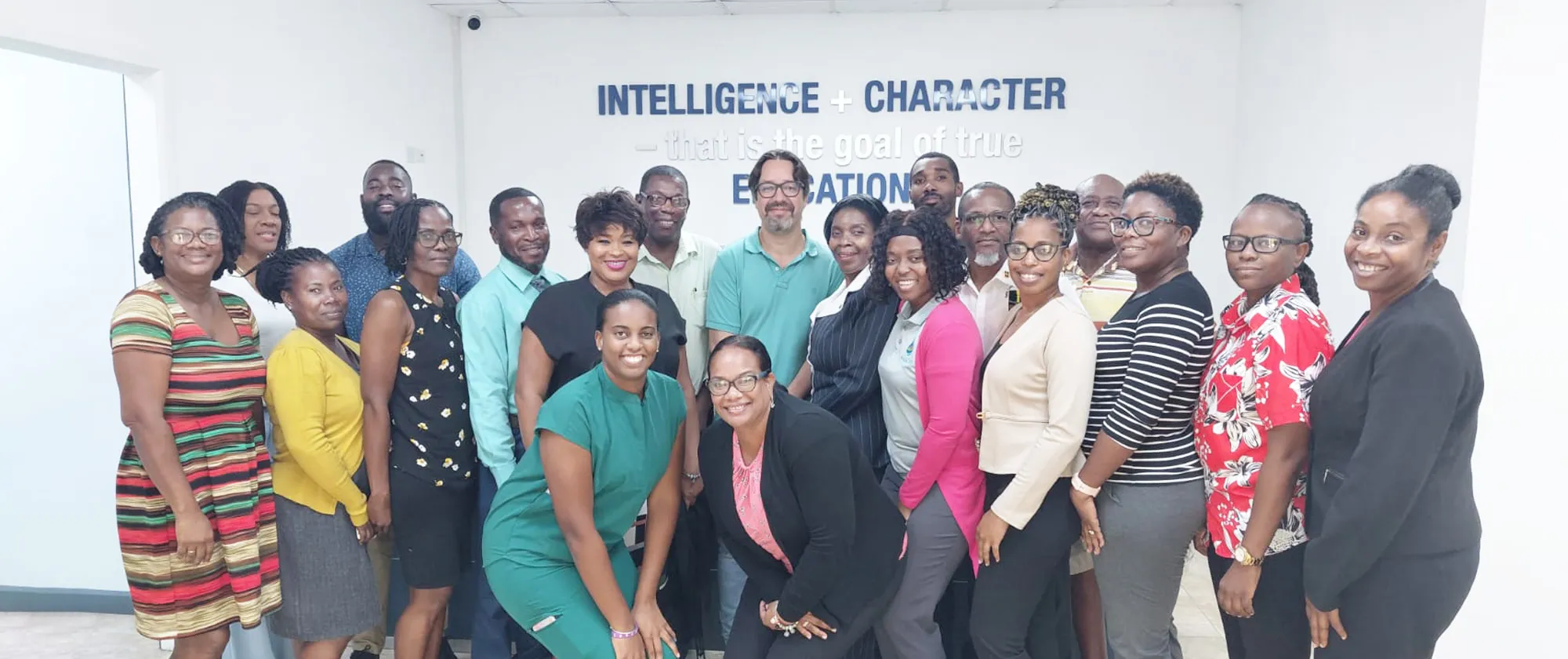 A group of approximately 20 diverse professionals standing together for a commemorative photo in front of a wall that reads, "INTELLIGENCE + CHARACTER — that is the goal of true EDUCATION."