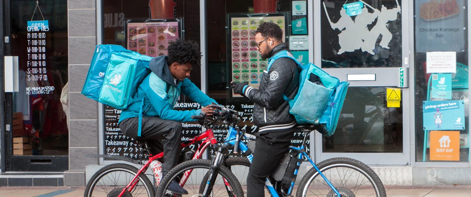 Two gig economy workers on bikes, checking their phones