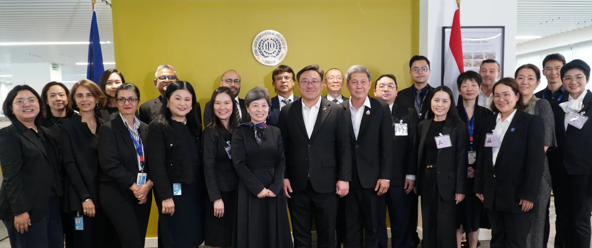 A group of officials and staff members pose for a formal photo in an office setting.