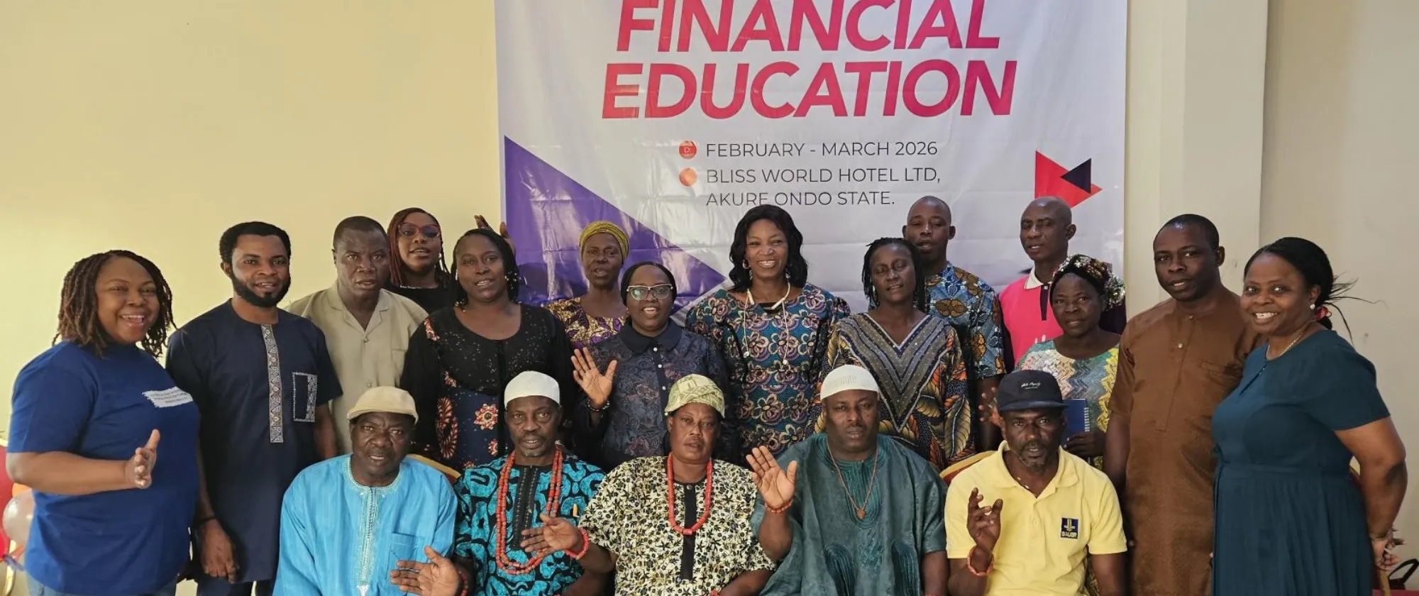A large group of training participants and facilitators stand and sit in front of a banner for the "Training of Beneficiaries on Financial Education" in Akure, Ondo State, smiling for a group photo.