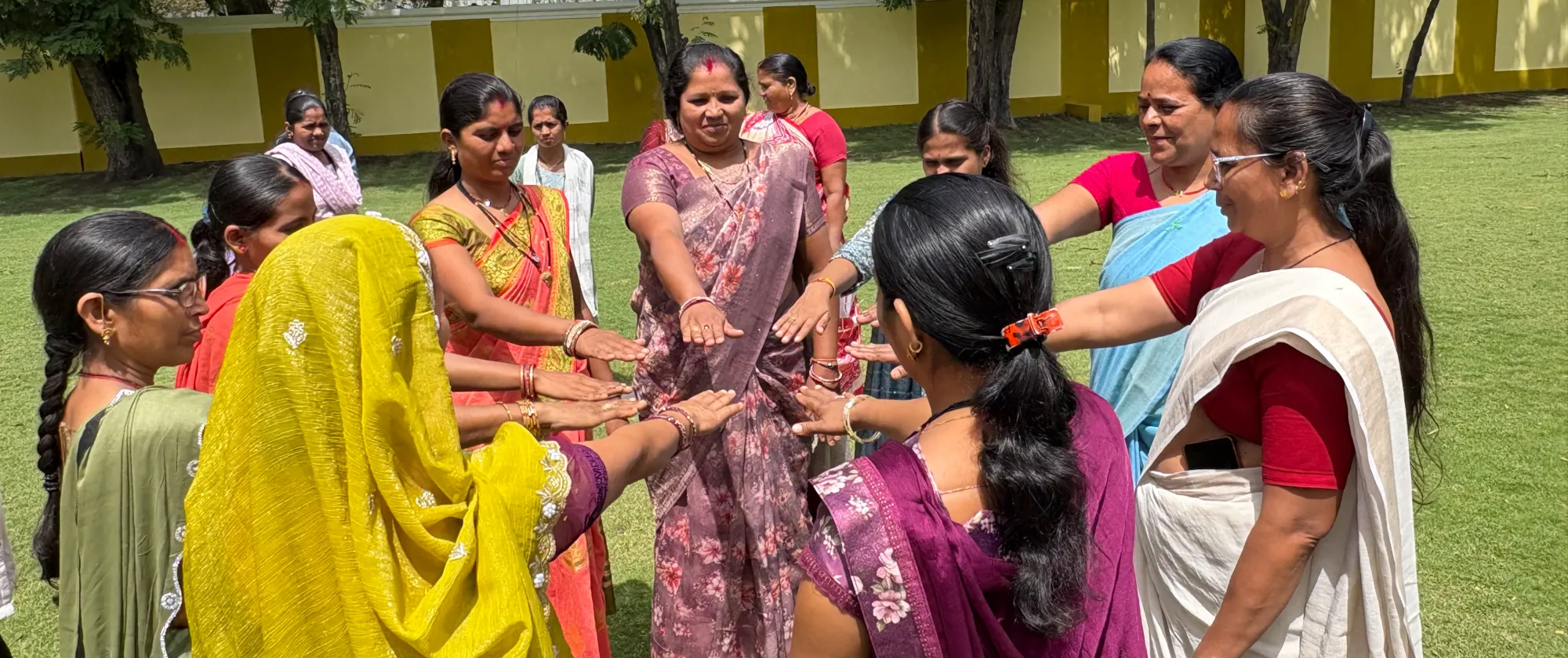 A group of women stand in a circle outdoors with their hands extended toward the center.