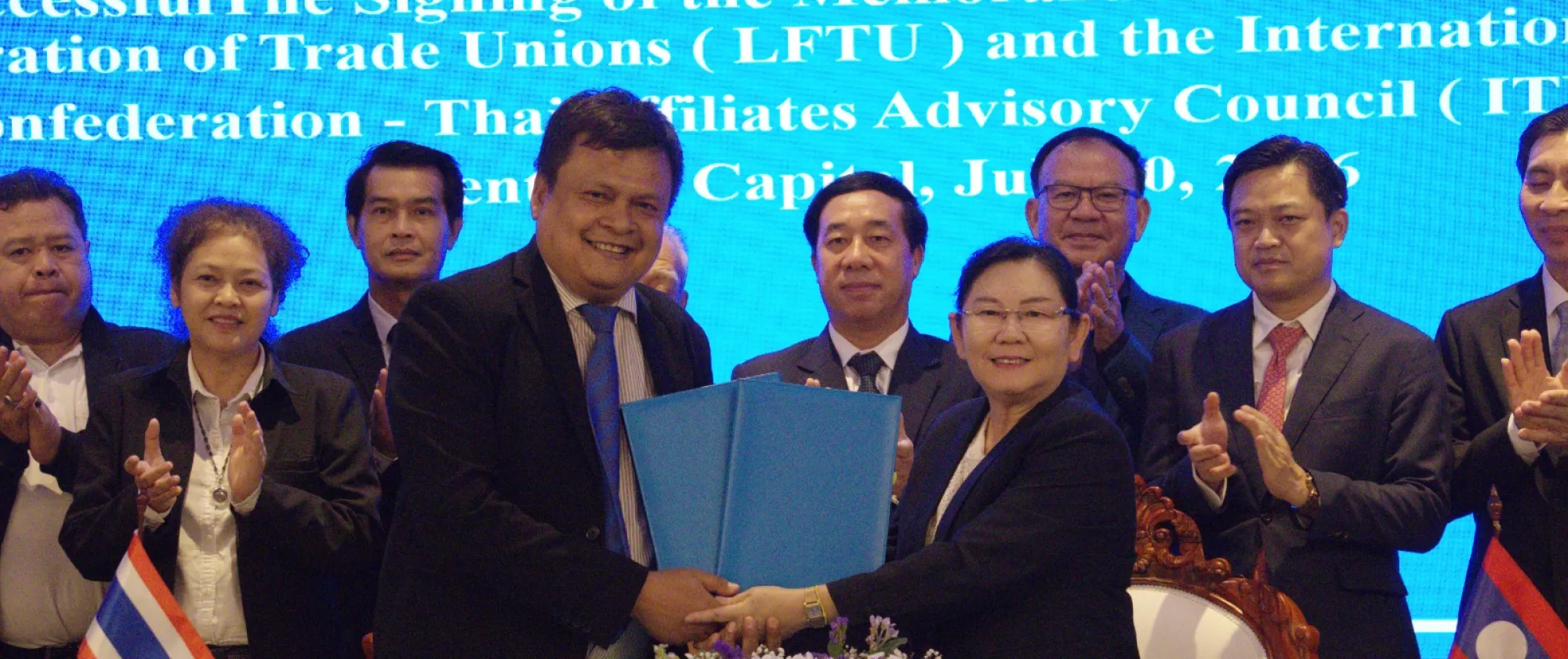 People shake hands with the flags of Lao PDR and Thailand displayed on the table.