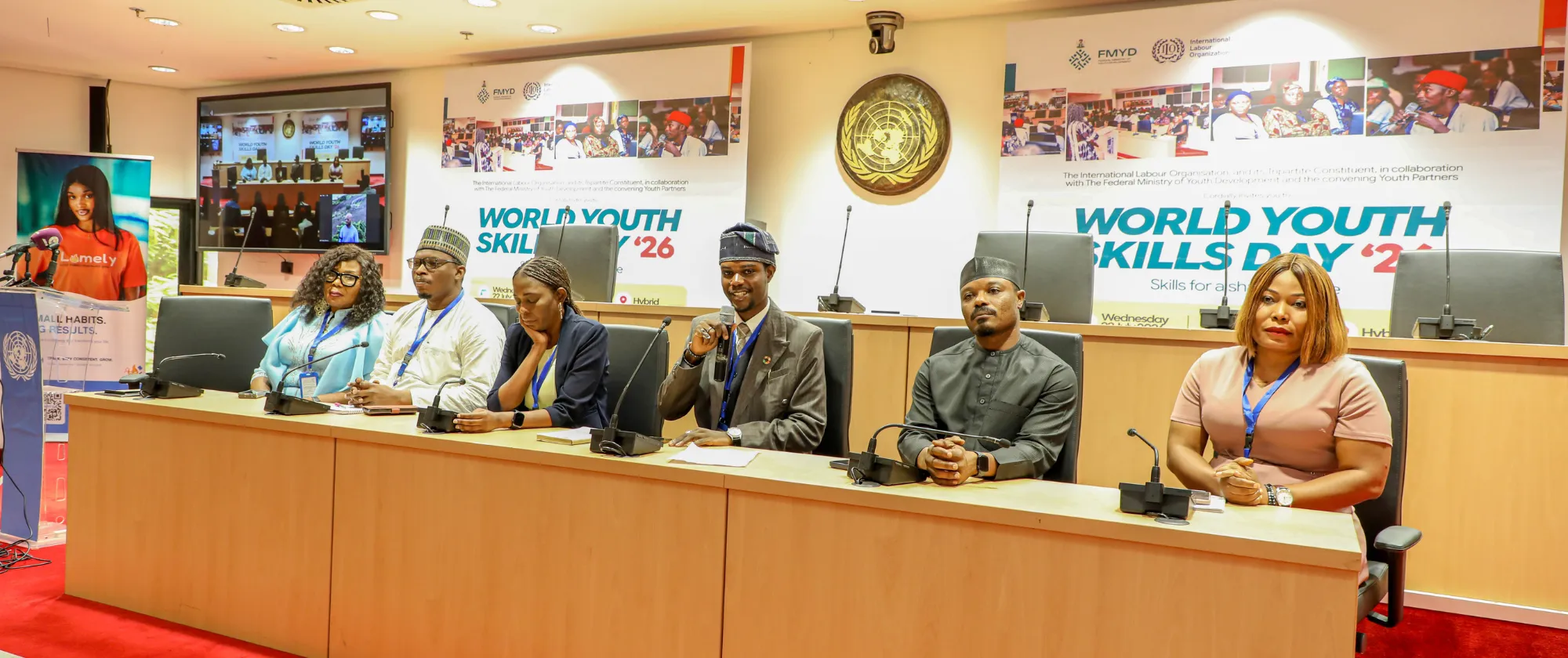 A panel of participants sits behind a long conference desk beneath World Youth Skills Day 2026 banners, while one panelist speaks into a handheld microphone.