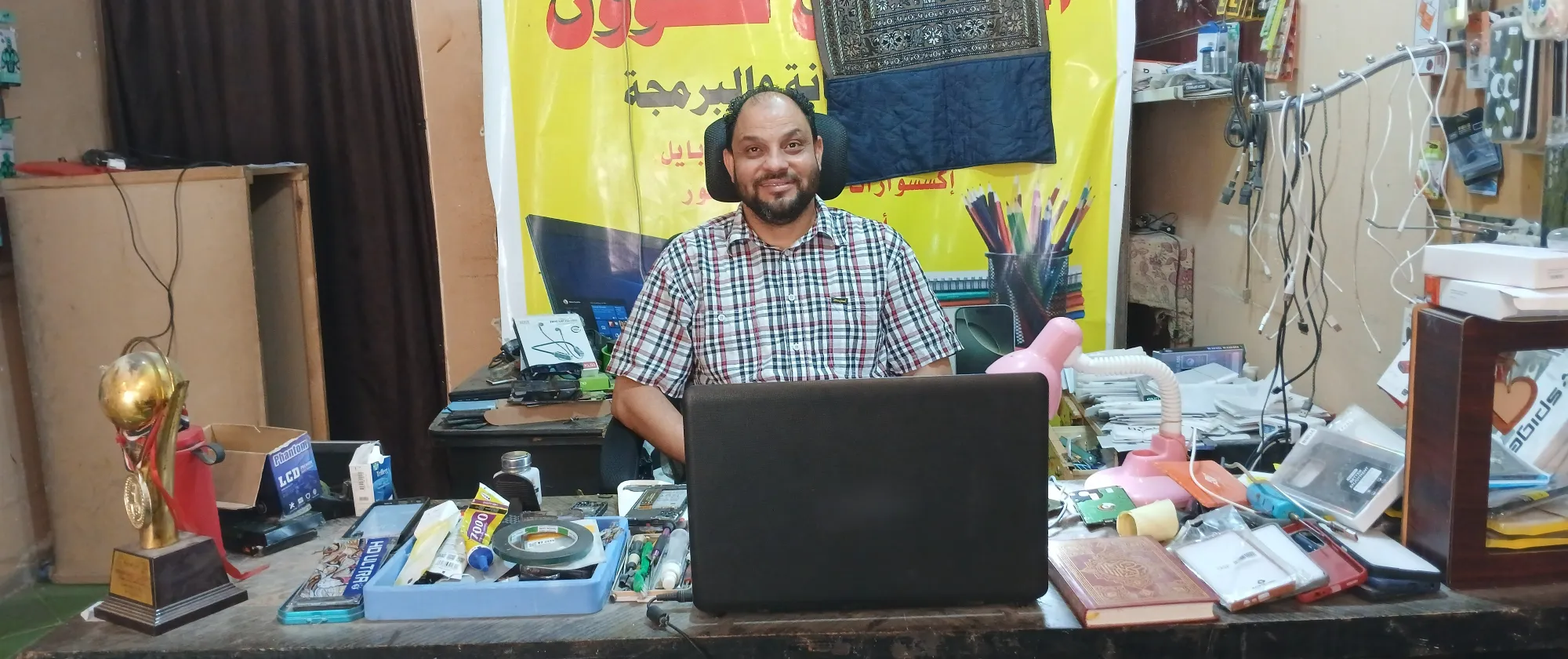 Alhassan Ali sits behind a desk in his mobile phone repair shop. 