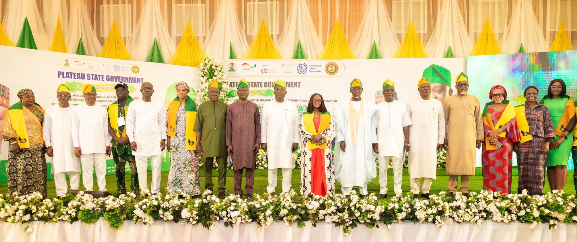 A group of government officials, ILO representatives and other stakeholders stand together on a decorated stage