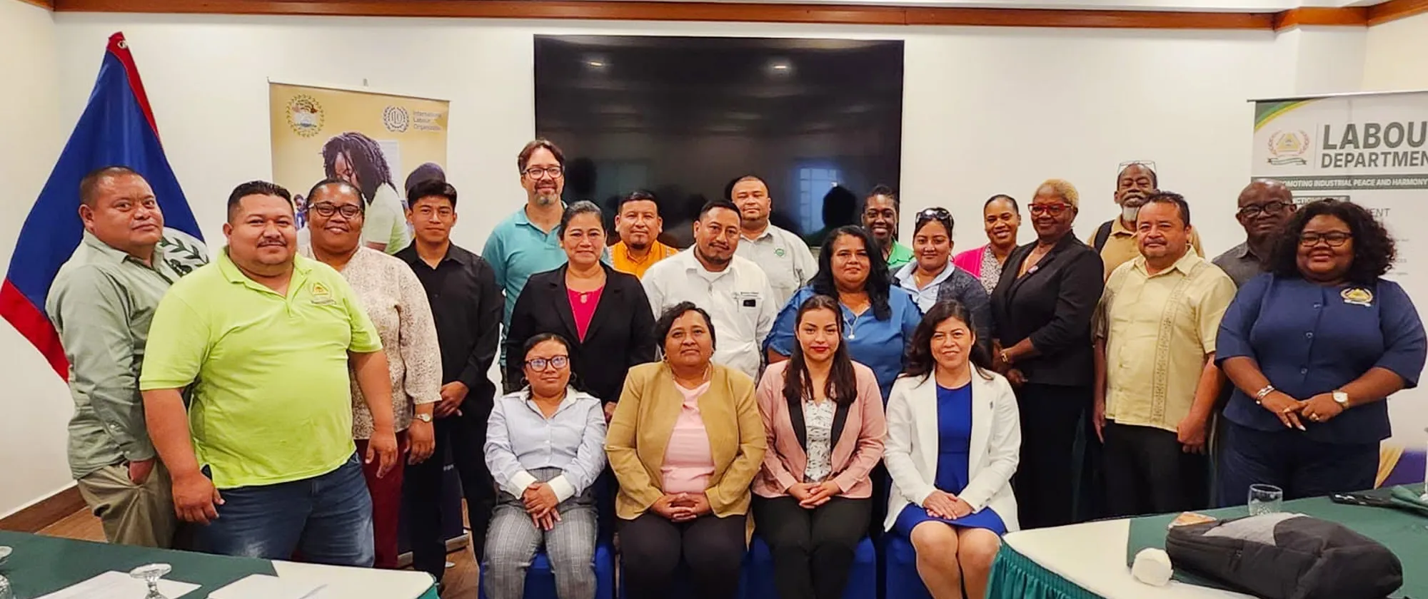 A group photograph of approximately 20 professionals attending a labour complaints tribunal event in Belize. The diverse group of men and women are dressed in professional and business casual attire, smiling at the camera.