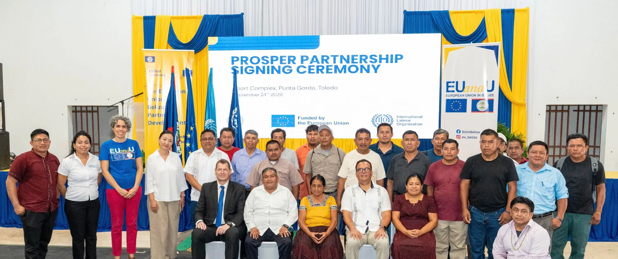 A group of persons standing in rows in front of a large sign