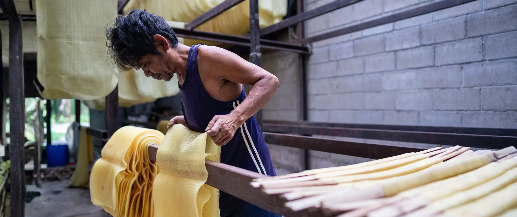 Phong, a worker in eastern Thailand, dried rubber sheets and prepared them for sale. The sheets are stacked in neat piles in a shed, awaiting collection by a trader.