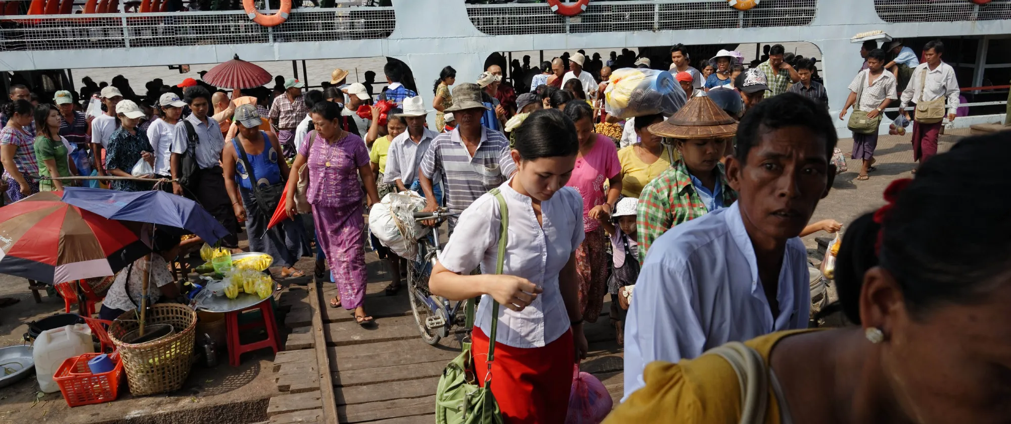 Crowds of people disembark from a passenger ferry at a busy riverside landing