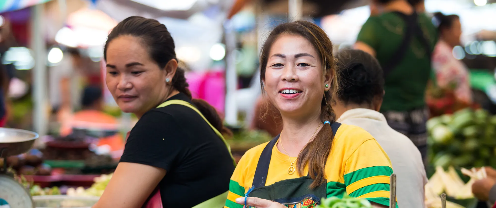 Two women sell fresh vegetables at a market. 