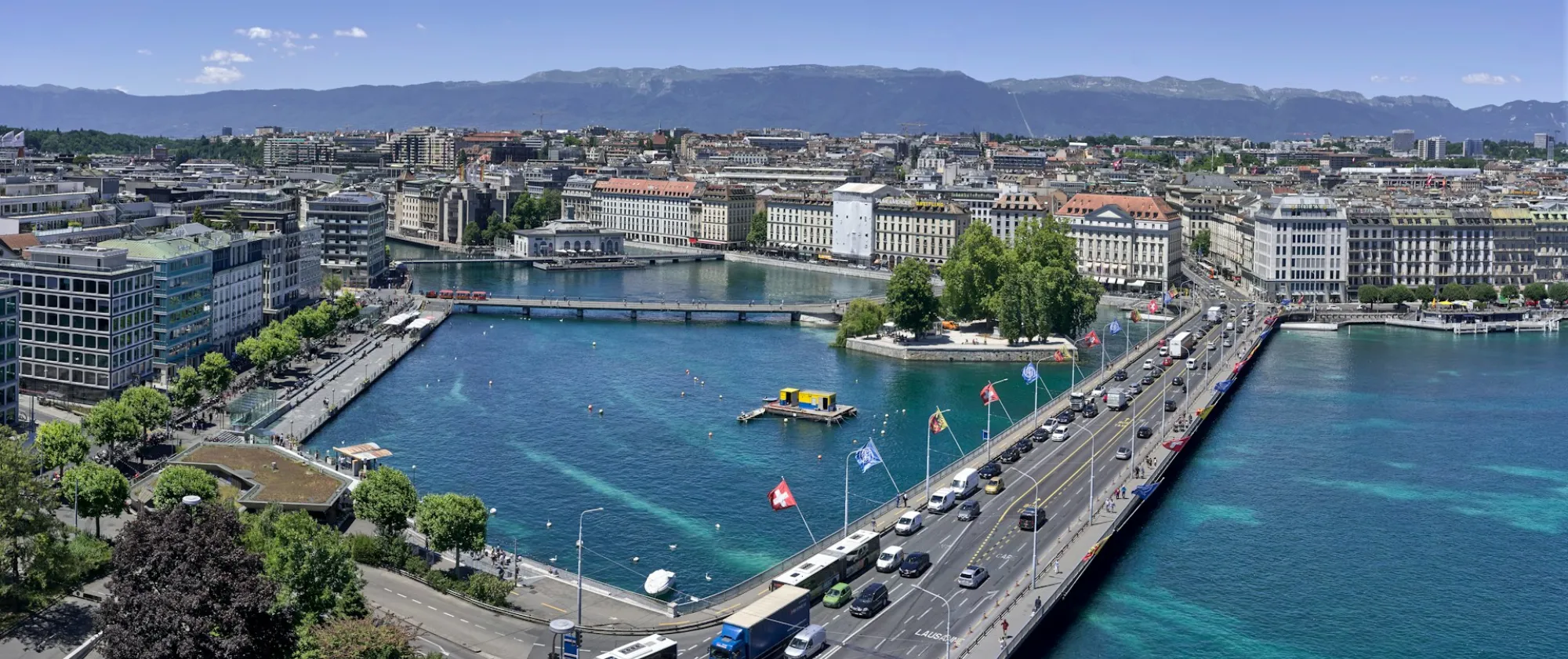 Panoramic view of central Geneva, with the Rhône flowing out of Lake Geneva beneath the Mont-Blanc Bridge and the Jura mountains in the distance.